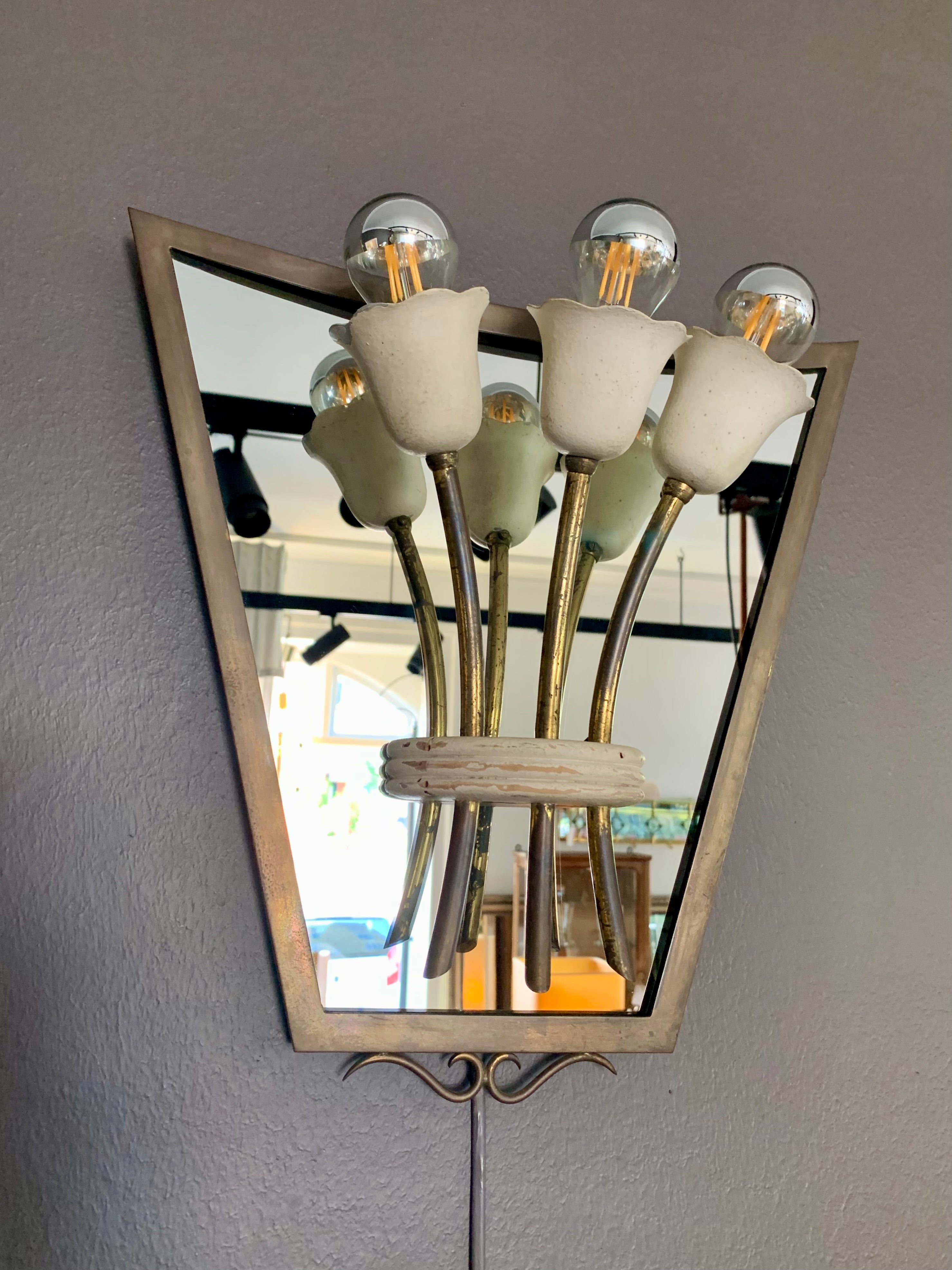 Fabulous set of four vintage brass and mirror wall lamps. Each of the 1940s shield shaped sconces has a mirrored background in a brass frame with a small bouquet of three tulips with a light source that. The charming sconces can either be connected