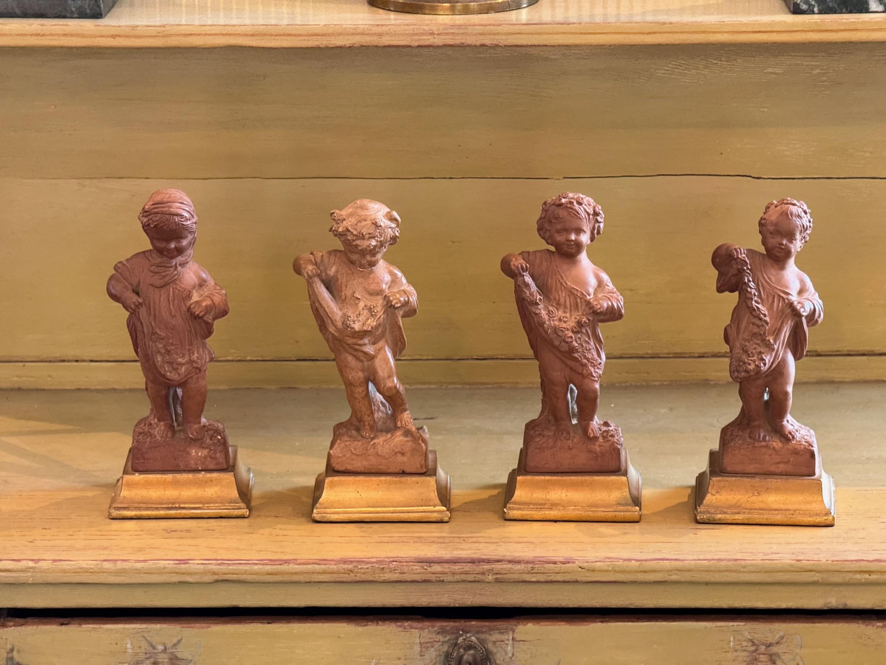 Conjunto de cuatro figuras Borghese de terracota que representan las Four Seasons, cada una modelada como un putto con motivos estacionales. La rica arcilla roja con bases de madera dorada añade calidez y contraste. Un conjunto decorativo de