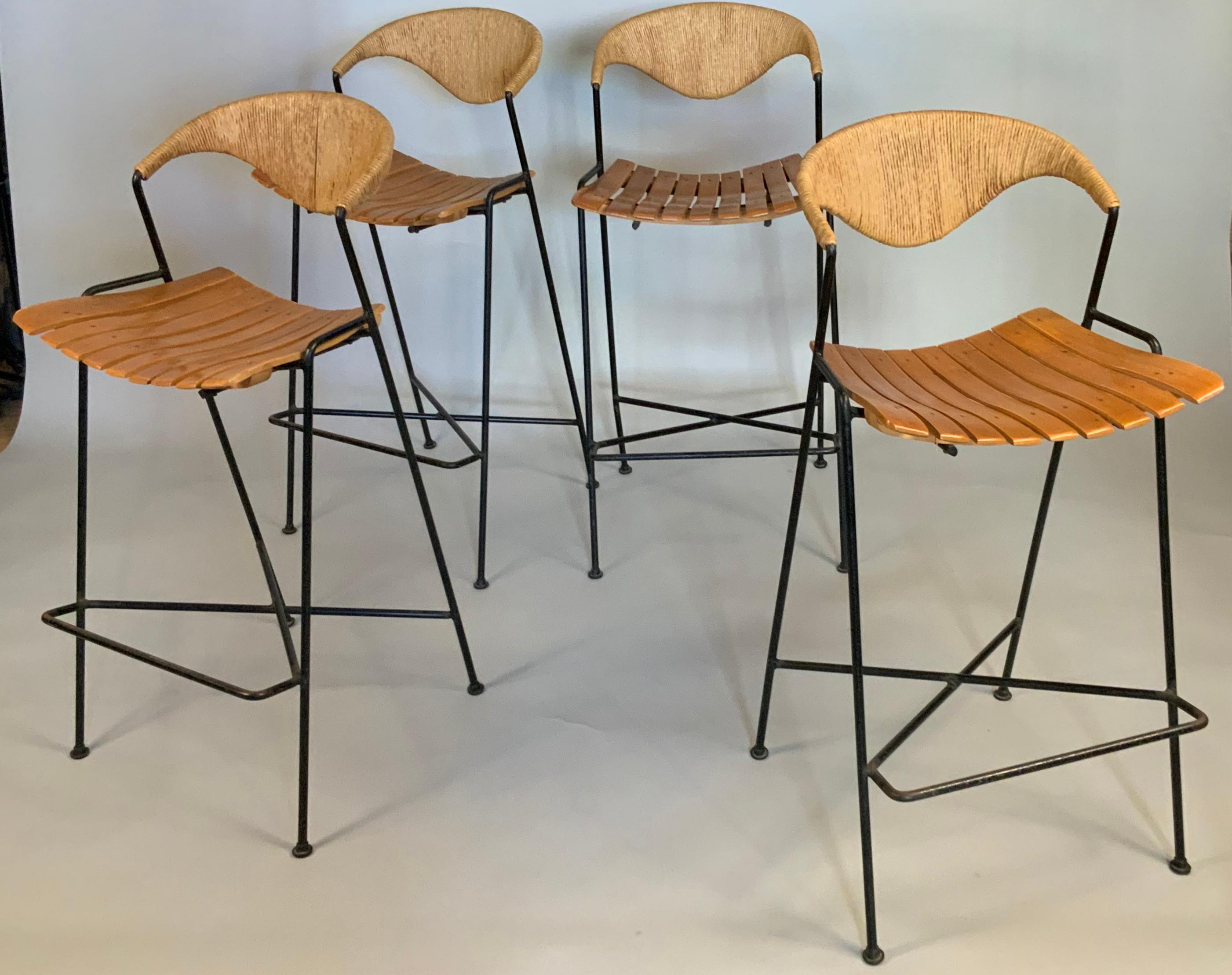 A set of four of the best Classic modern, 1950s barstools designed by Arthur Umanoff. sturdy wrought iron frames with footrest, and a sculpted slat seat in birch, and backs of woven rope. Incredibly comfortable, stylish, and well made.
