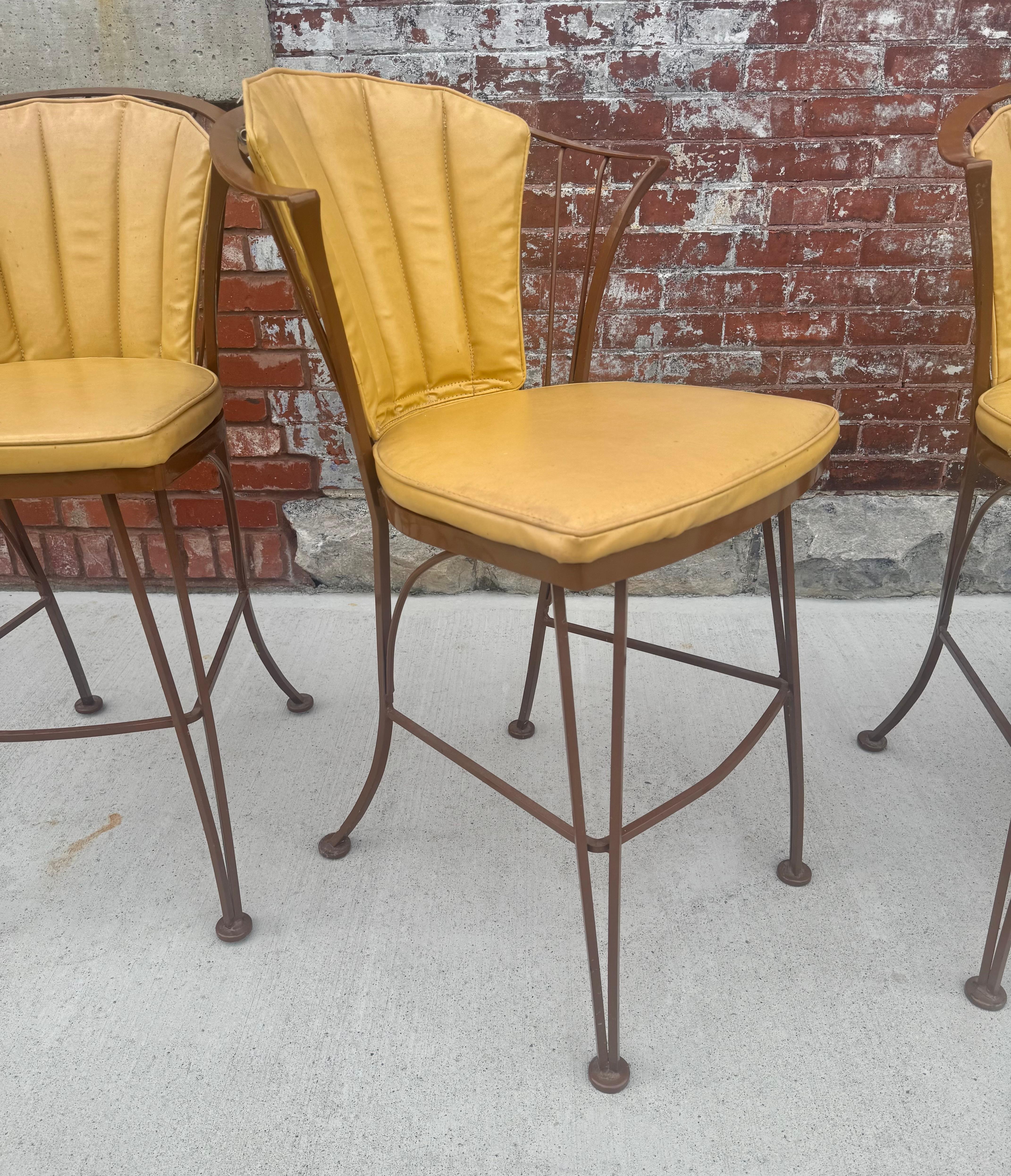A set of four vintage 1950s wrought iron barstools from the Pinecrest collection by Woodard. Beautiful stylish design with curved legs and back and original seat and back cushions in yellow -gold naugahyde,, Wonderful original condition..