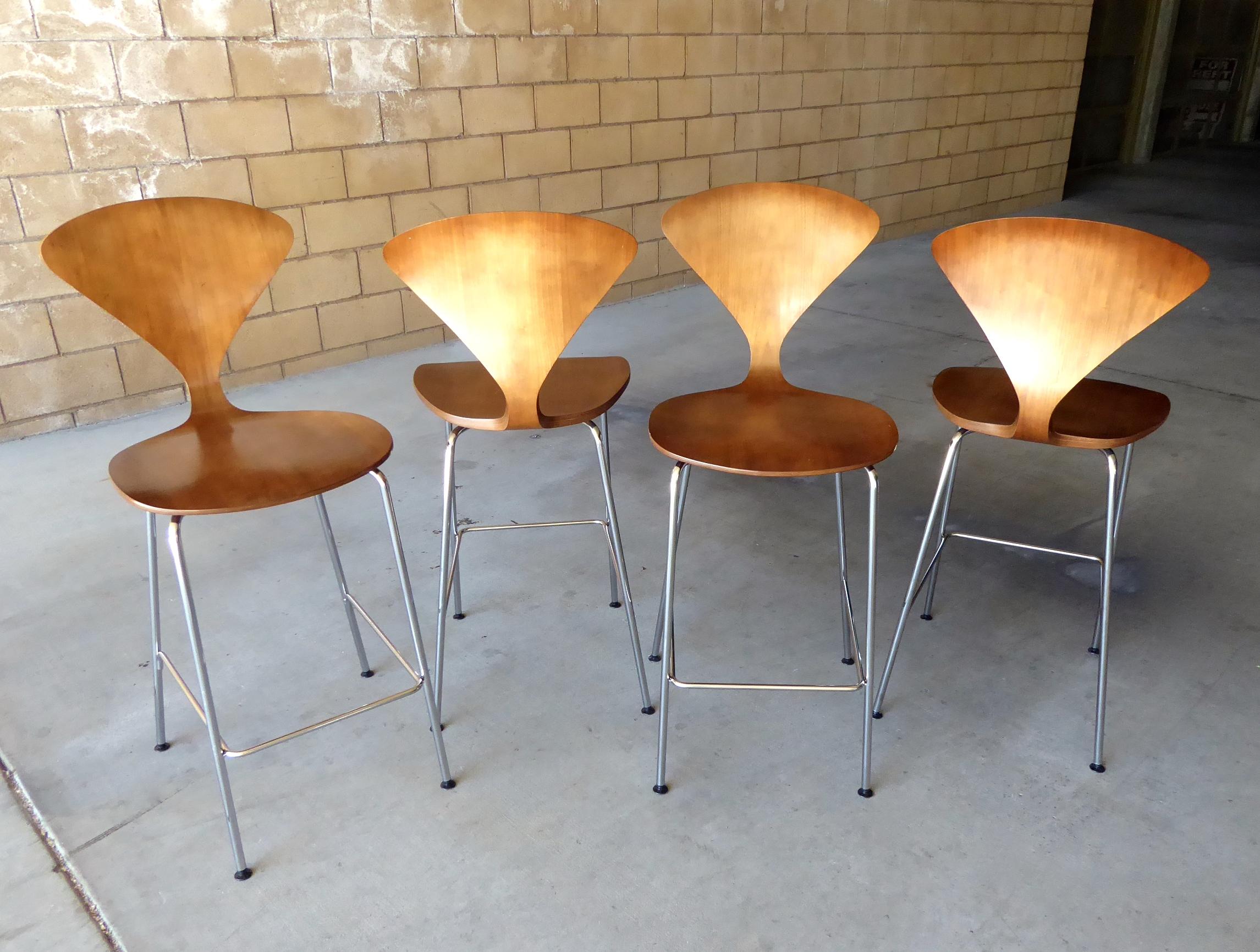 A set of four metal based counter stools with molded Classic-walnut plywood seats by Norman Cherner manufactured in 2010. This set of stools was acquired from a home in Palm Springs.
 