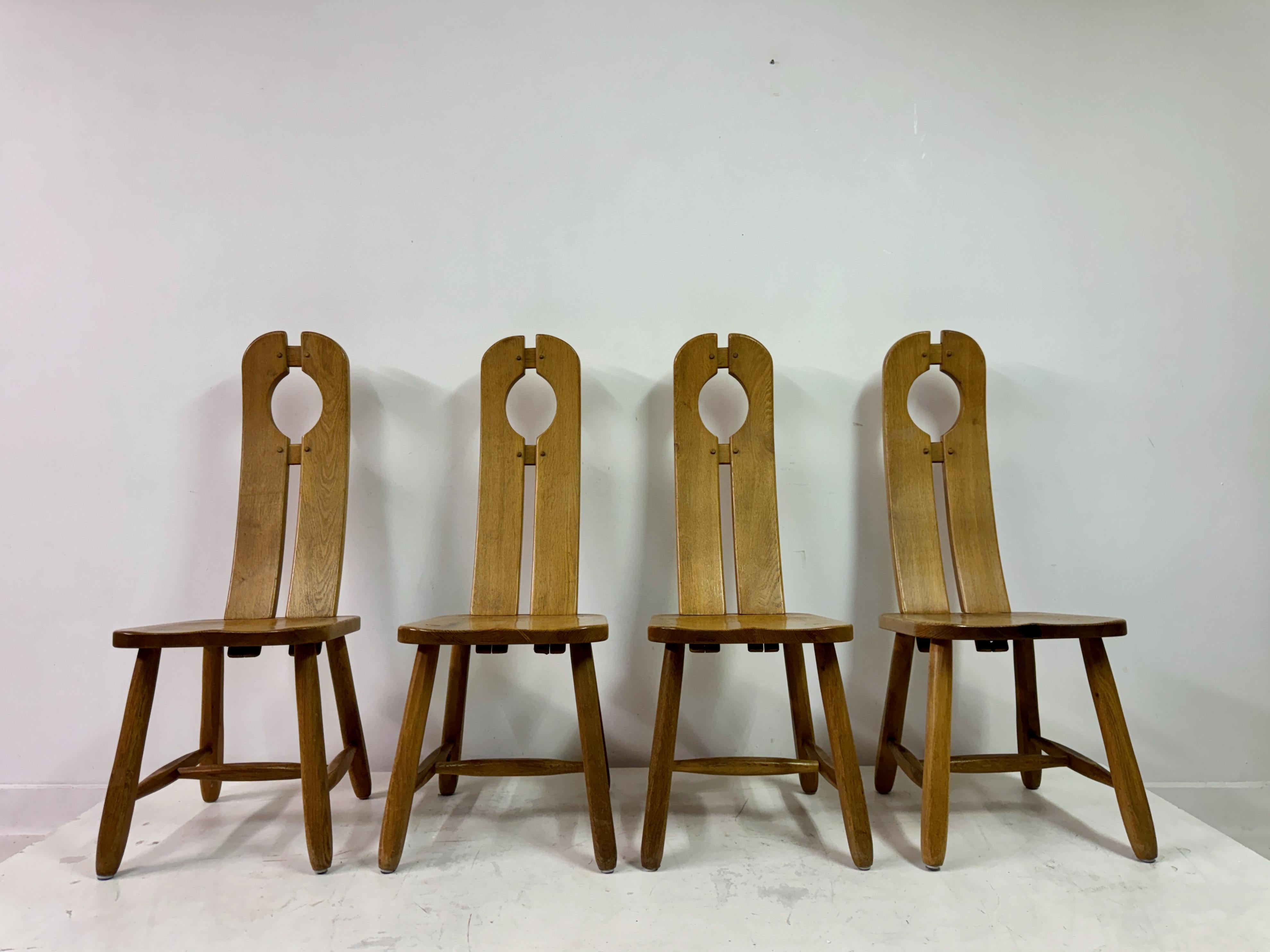 Set of four oak dining chairs by De Puydt

This is a set of four solid oak dining chairs featuring a distinctively rustic and modern design. Each chair showcases a tall, curved backrest with a central circular cut-out near the top, adding an element