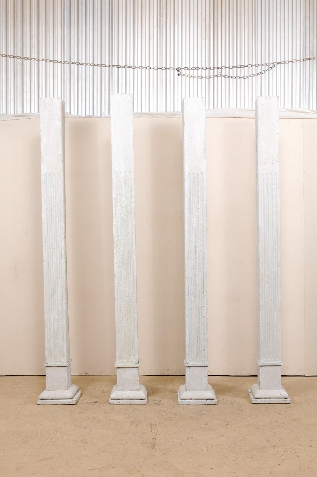 A tall set of four 19th century painted wood columns. This set of antique American pillars, standing over 8.5 feet in height, have square-shaped bodies with carved fluting, and are raised upon graduated and square-shaped bases. The columns are