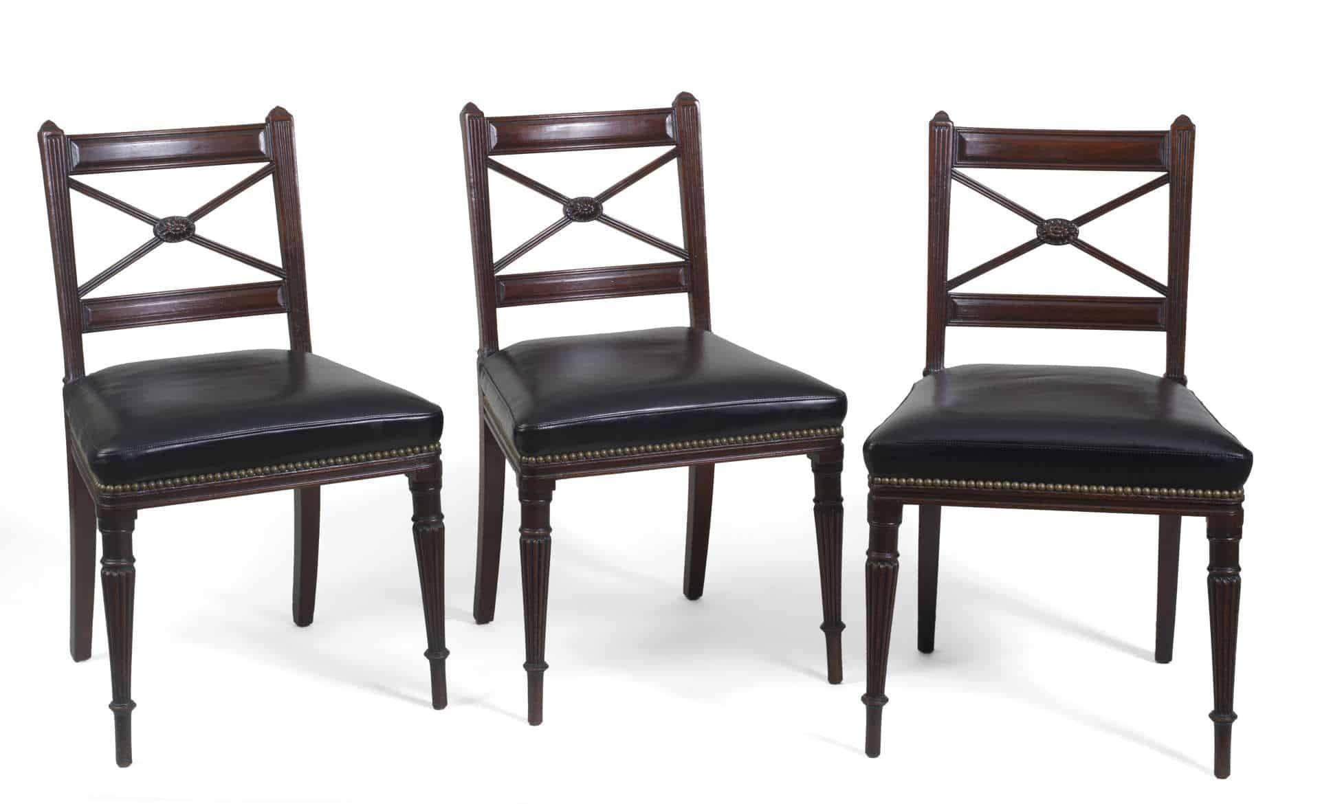 Set of four (4) 19th century English carved mahogany side chairs; straight crest rail above an X-form and oval flowerhead patera splat, black leather seat and nailhead trim raised on frontal turned and tapered reeded legs.