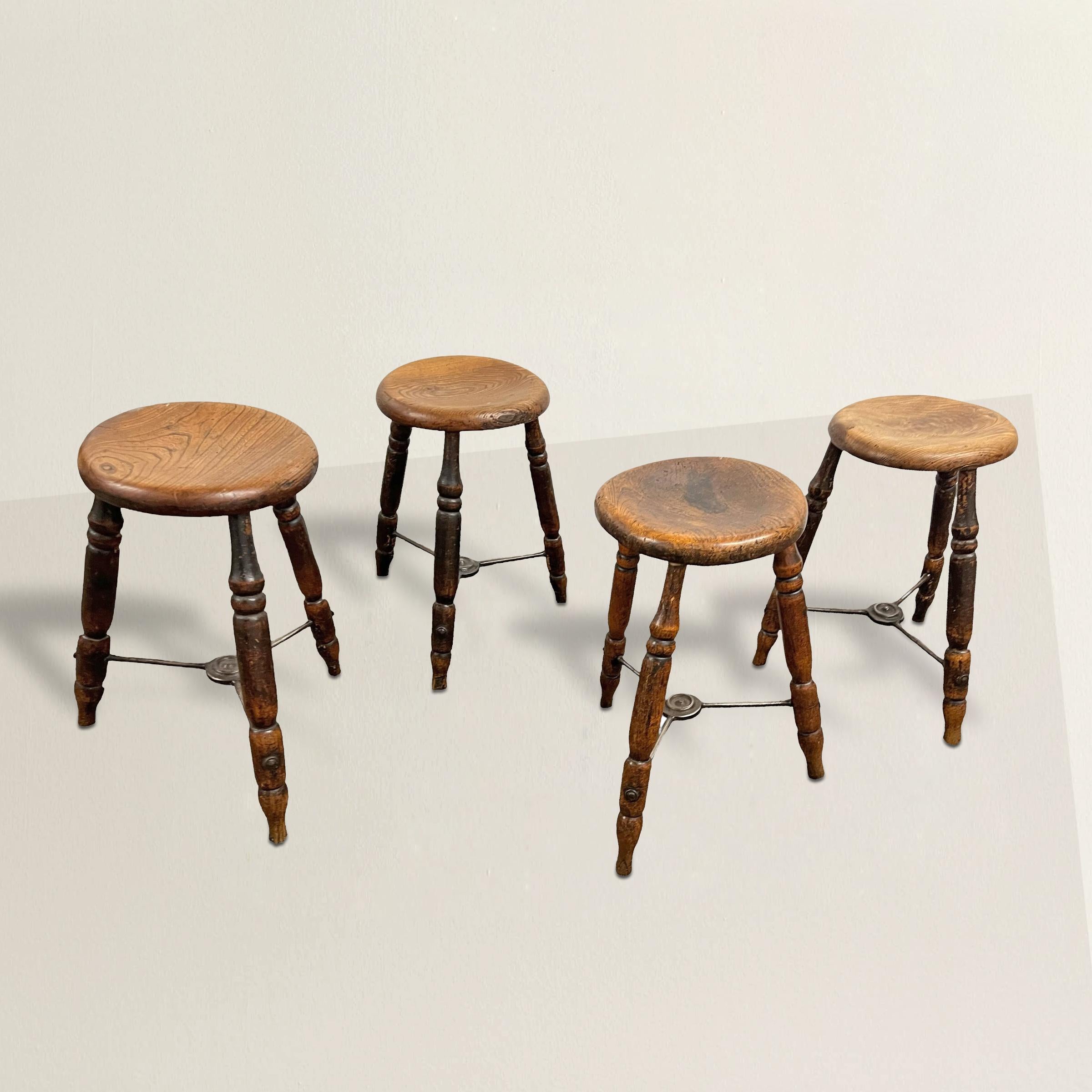 Embrace the rustic charm of late 19th-century England with this set of four pub stools, each a treasure of timeless appeal. Crafted from sturdy elmwood, their seats bear the marks of generations of use, boasting a patina that speaks volumes of