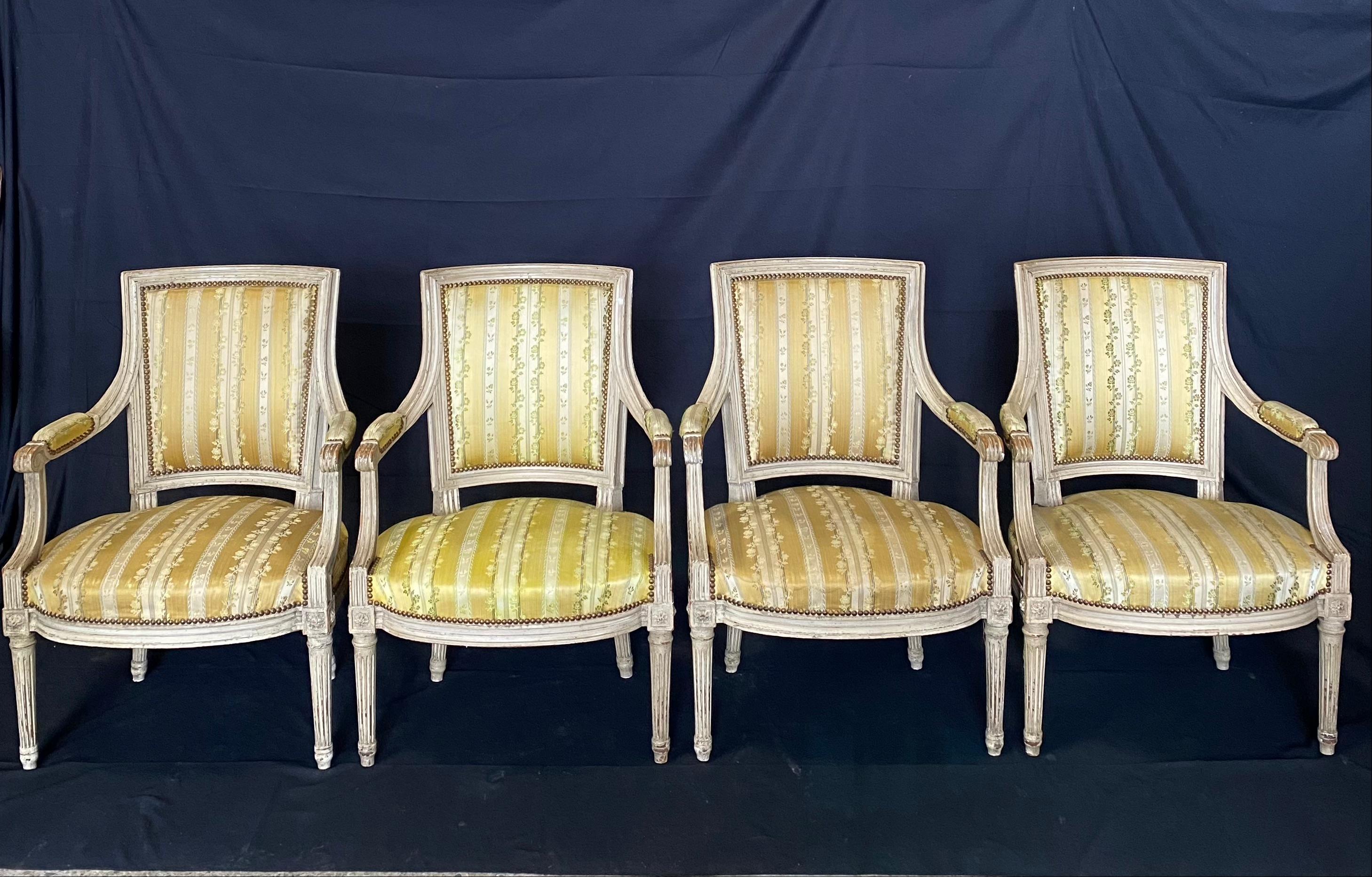 19th century painted Louis XVI armchairs with tapered fluted legs, bow front seats, square upholstered padded back, and upholstered arms, all in classic French gold striped fabric. Fabric is in good shape and probably original to the chairs. One of