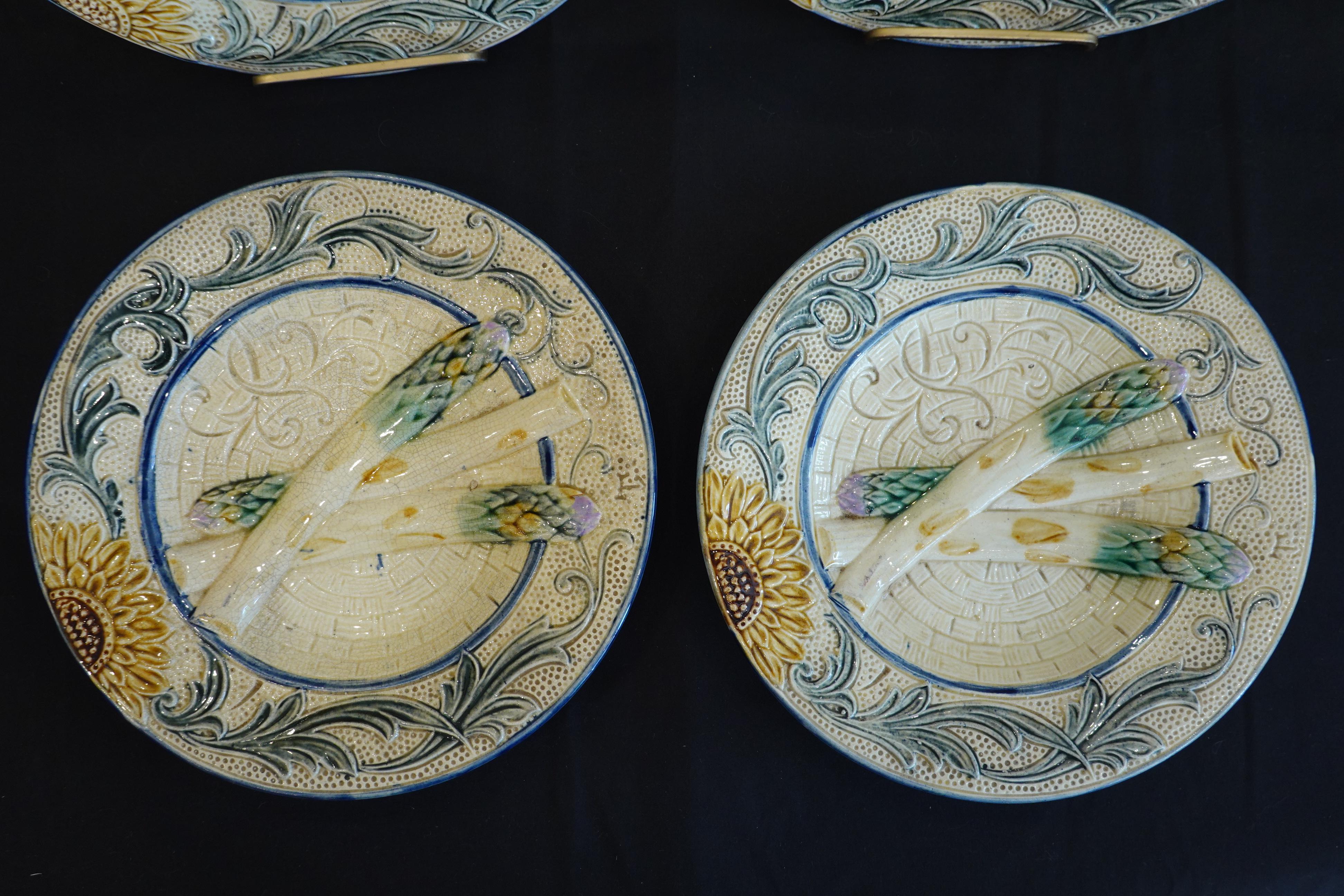 Satz von vier Majolika-Spargeltellern aus dem 19. Jahrhundert. Auf jedem Teller befinden sich drei geformte Spargelstangen mit einer Sonnenblume und Ranken, die den Rand umschließen. Die Teller sind nicht beschriftet, aber einige haben einen