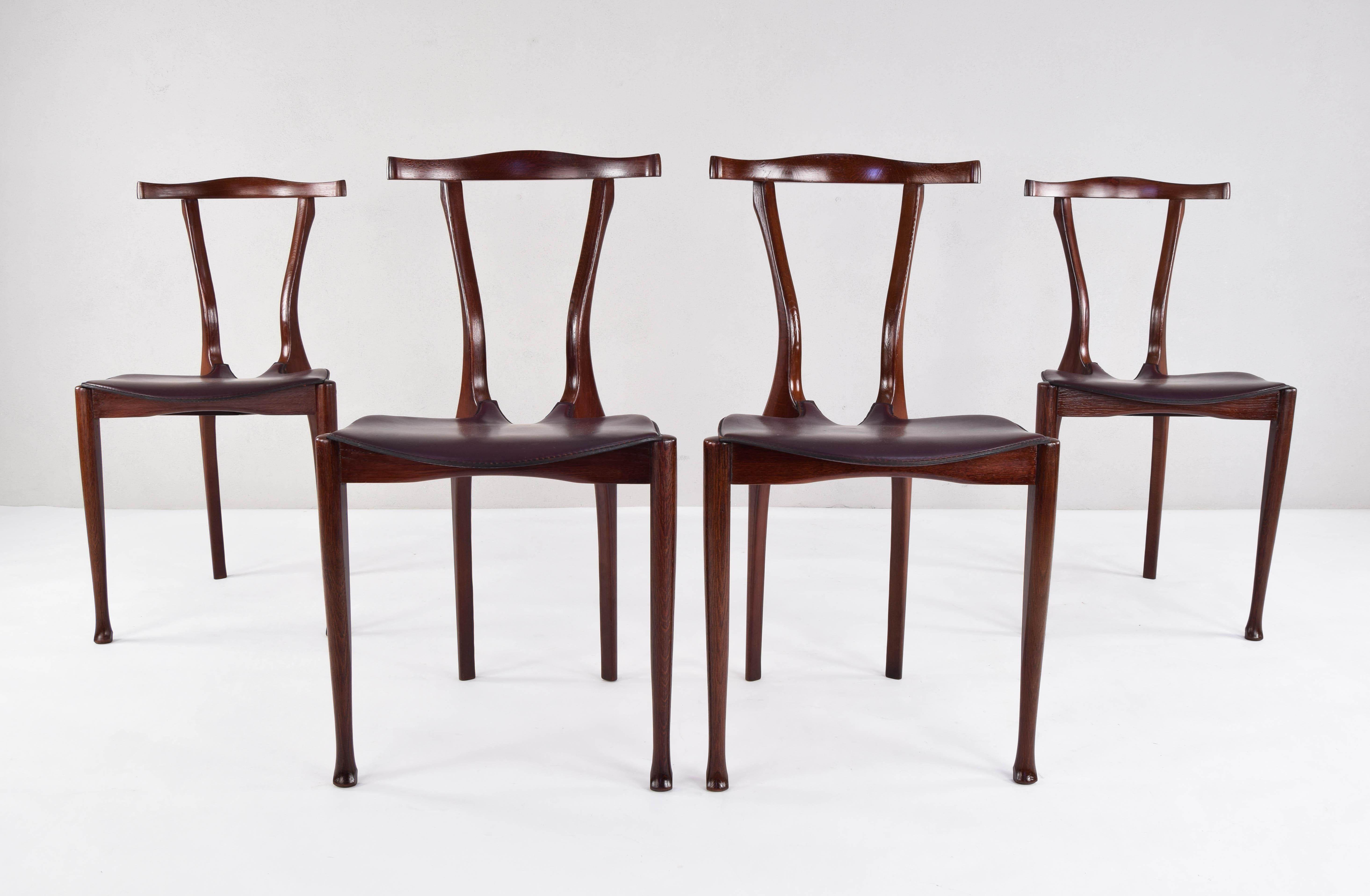 Set of four sculptural Gaulino chairs designed in 1987 by Oscar Tusquets in tribute to the works of Gaudí and Carlo Mollino. 
This is an original 1st production set made by Carlos Jané in stained oakwood and leather. Only the armchairs have been