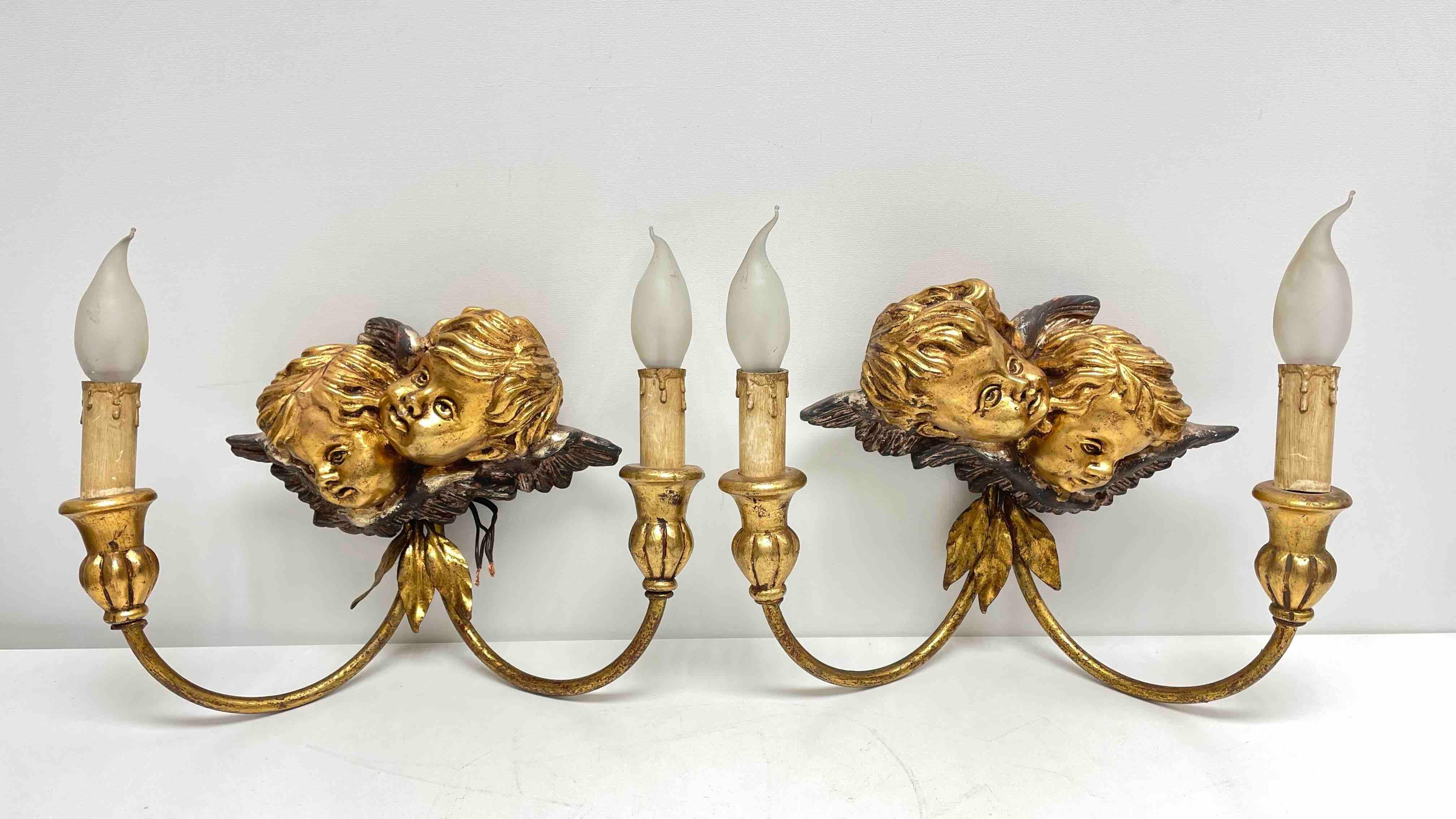 Two pair Hollywood Regency midcentury gilt tole sconces with wooden hand carved cherub angel heads, each fixture requires two European E14 candelabra bulbs, each bulb up to 40 watts. The wall lights have a beautiful patina and give each room a