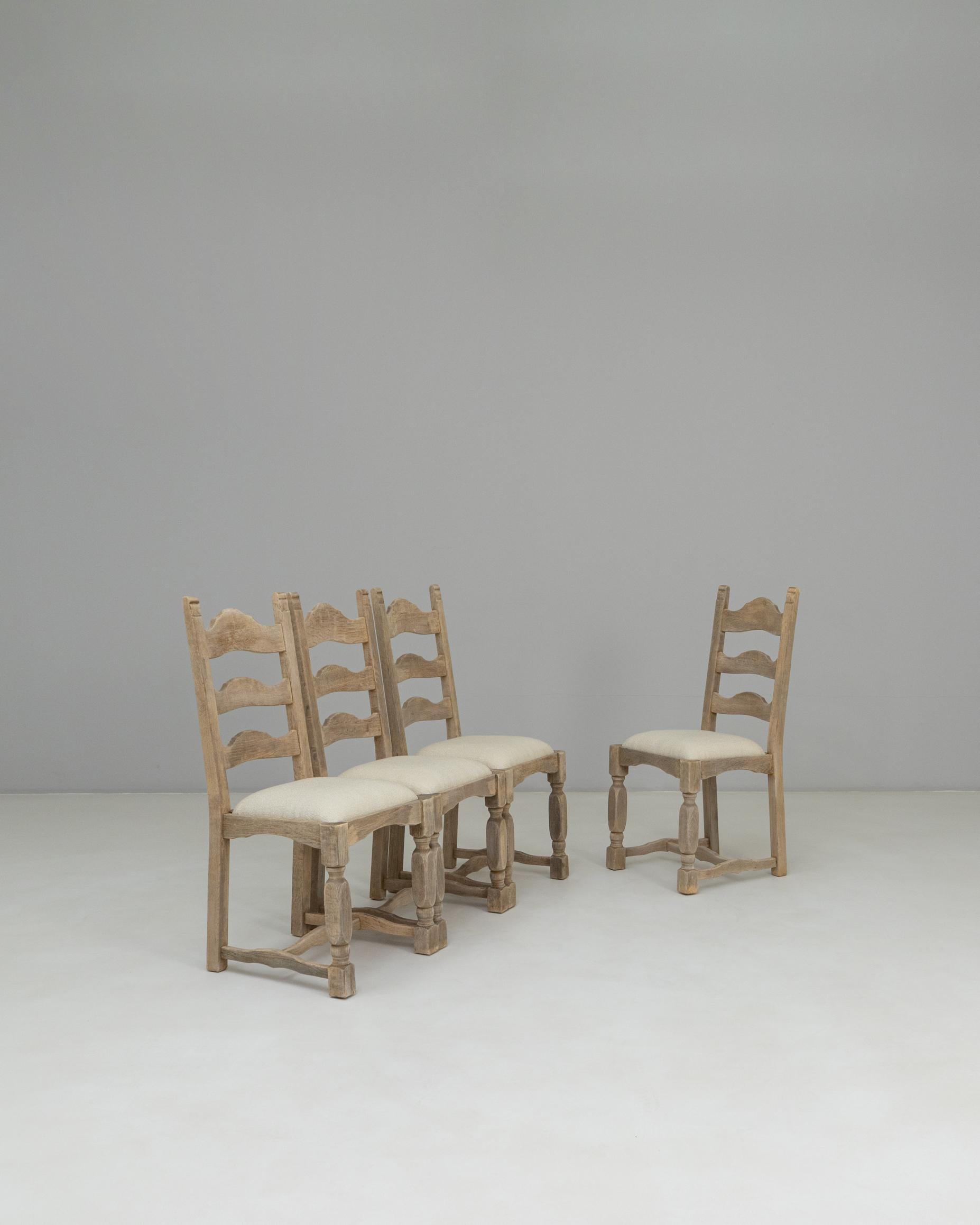 Este juego de cuatro sillas de comedor francesas de roble del siglo XX muestra una encantadora estética provinciana, con respaldos de escalera bellamente tallados y robustas patas torneadas. Los marcos de roble presentan una pátina suave y