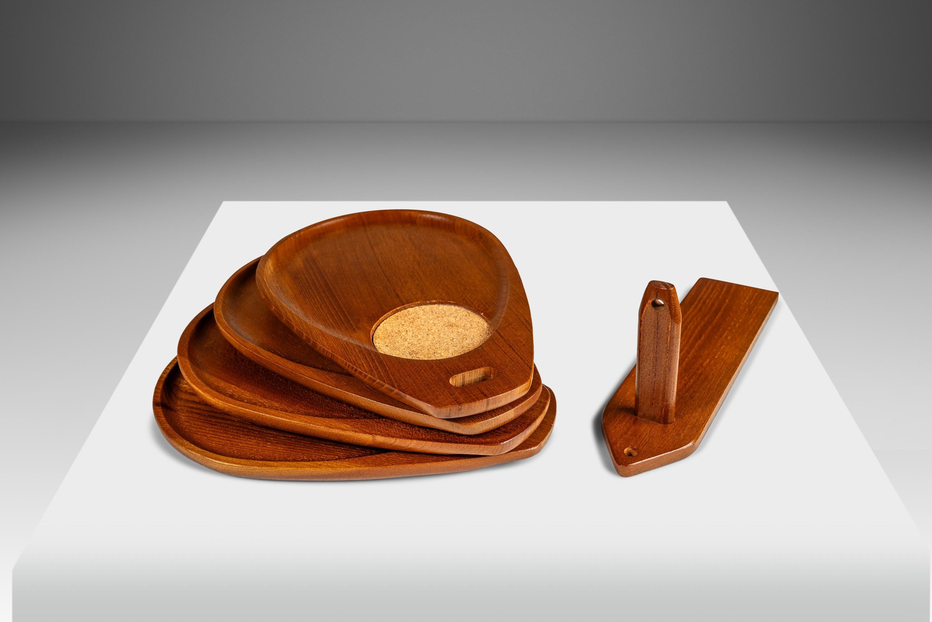 Introducing a splendid set of Japanese-made Mid-Century Modern serving trays with accompanying wall hanger all carved from solid slabs of solid Burmese teak with exquisite old-growth woodgrains throughout. With thoughtful cork drink coasters carved