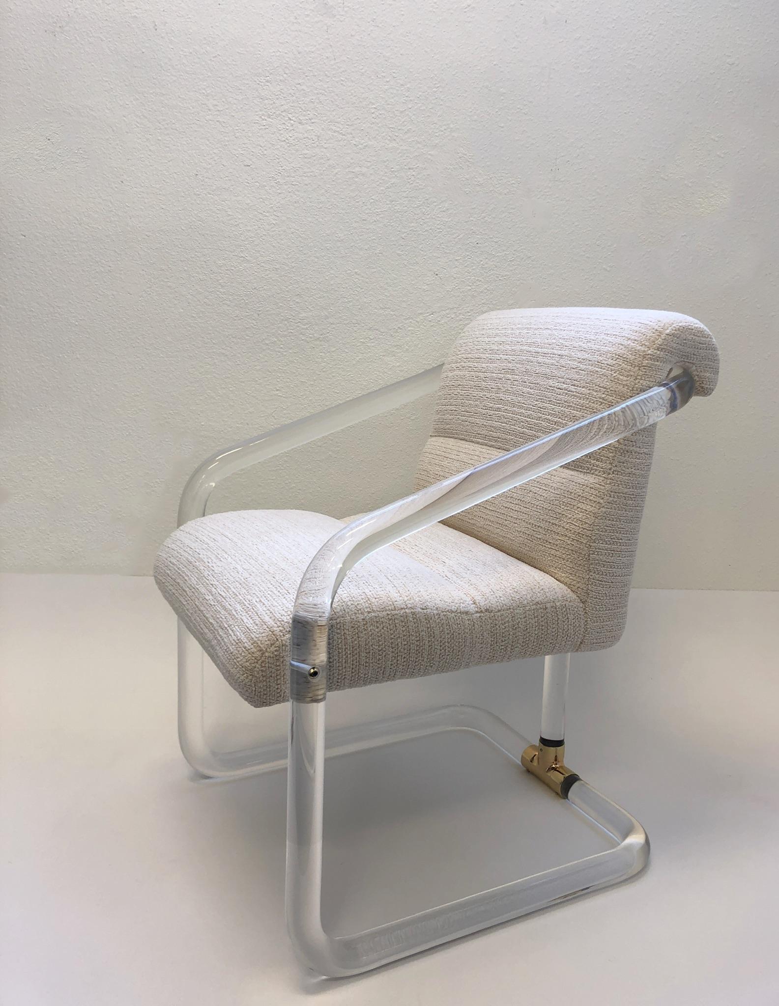 A glamorous set of four 1970s clear acrylic and polish brass arm chairs by Lion in Frost. This chair have been newly professionally polished and recovered in a beautiful off white channel fabric. All four chairs are signed Lion in