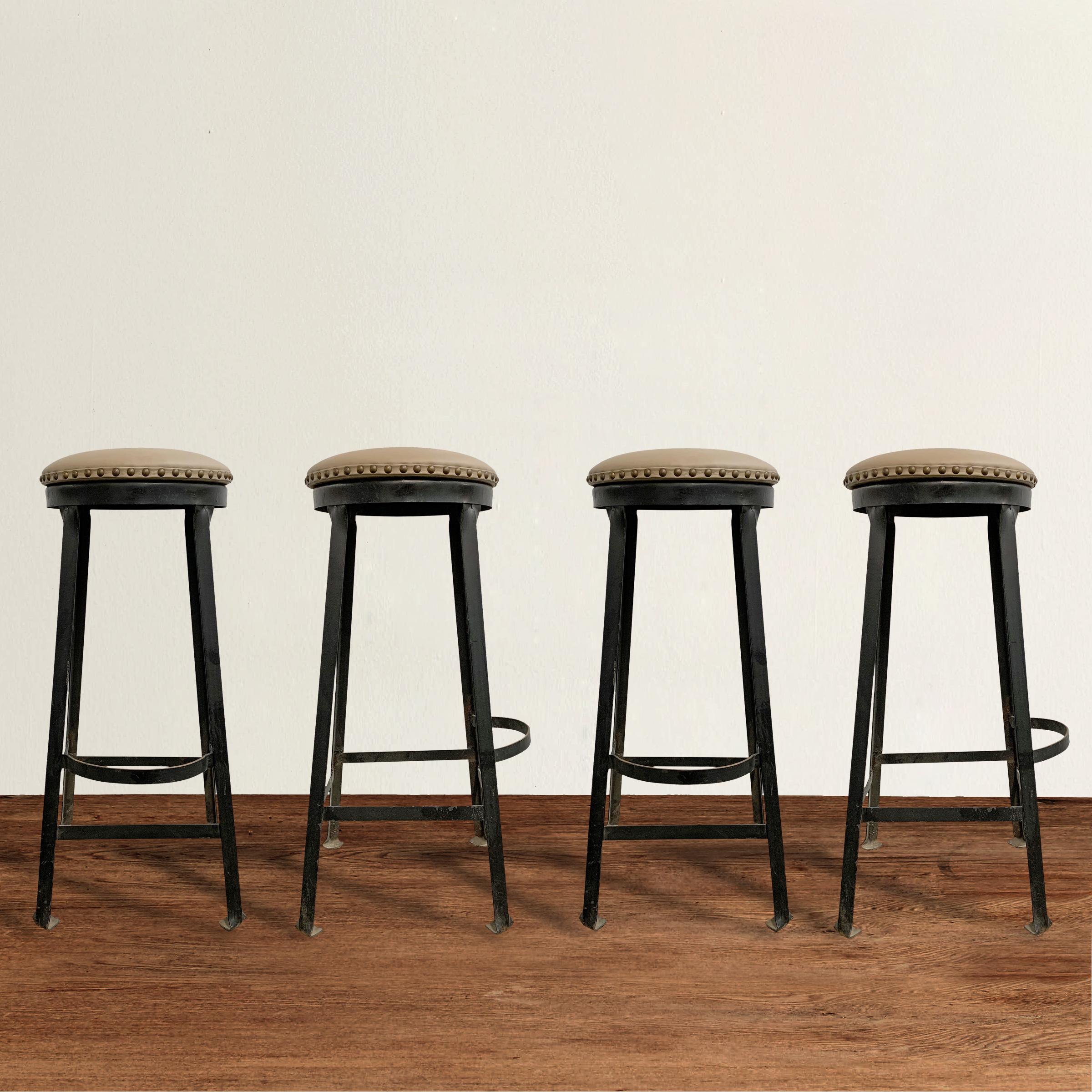 A smart set of four vintage American Industrial iron bar stools with foot rests, bent-stock feet, and newly upholstered in a beautiful taupe leather with brass nailhead trip.