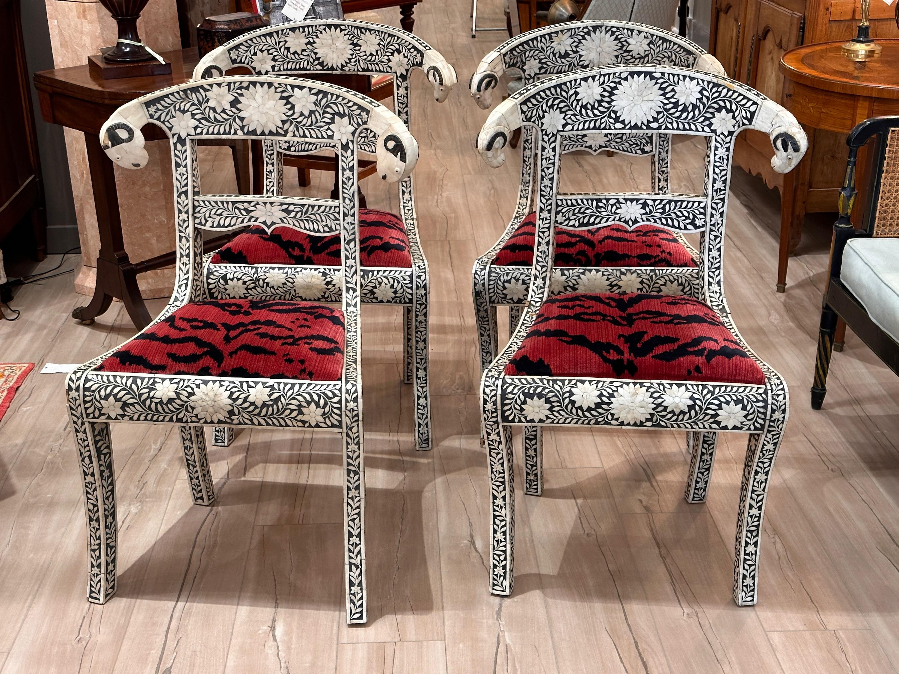 An set of four Regency style side chairs extensively inlaid with bone and ebony and carved ram's head accents upholstered in a red and black tiger stripe velvet.