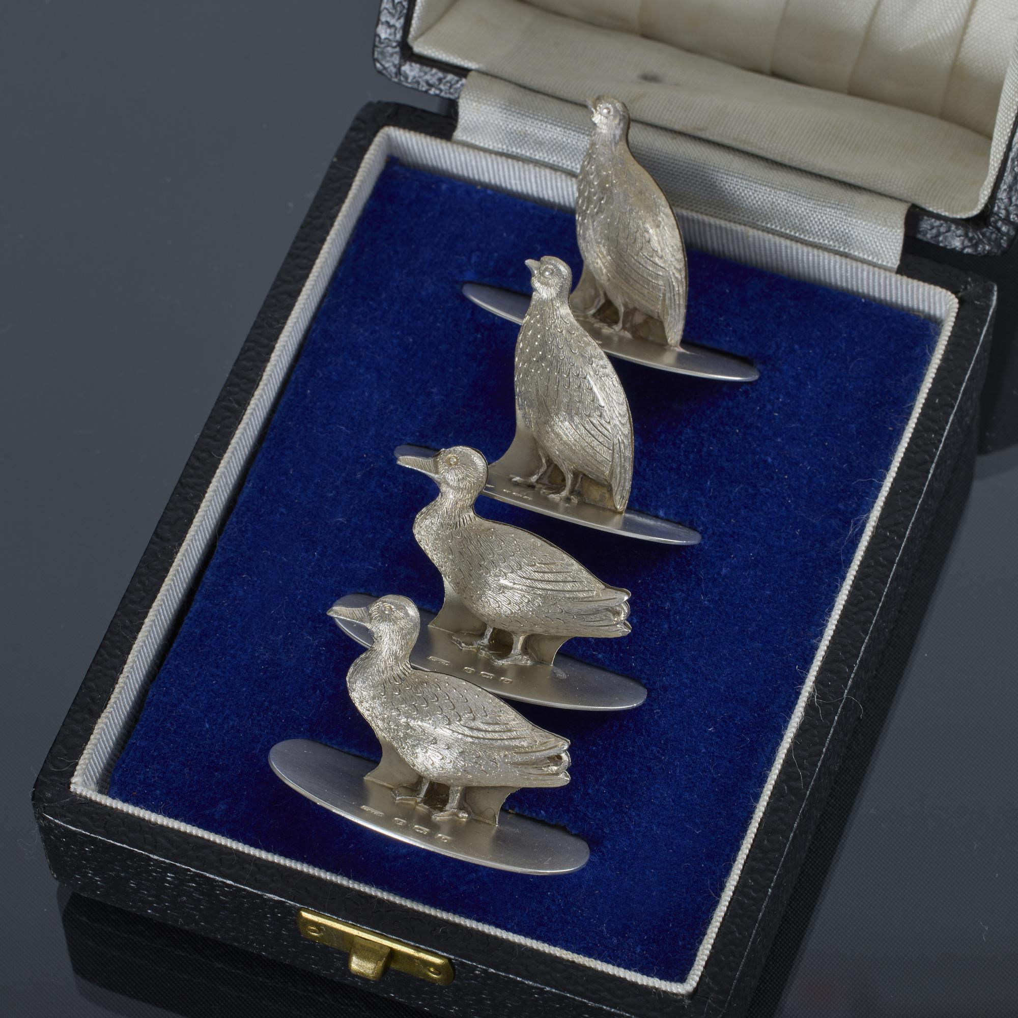 Ensemble de quatre porte-menus ou porte-cartes de table en argent ancien du début du XXe siècle, en forme de canards et de perdrix/souris/pintades, dans leur coffret de présentation d'origine.

Chaque porte-menu en argent est monté sur une base en
