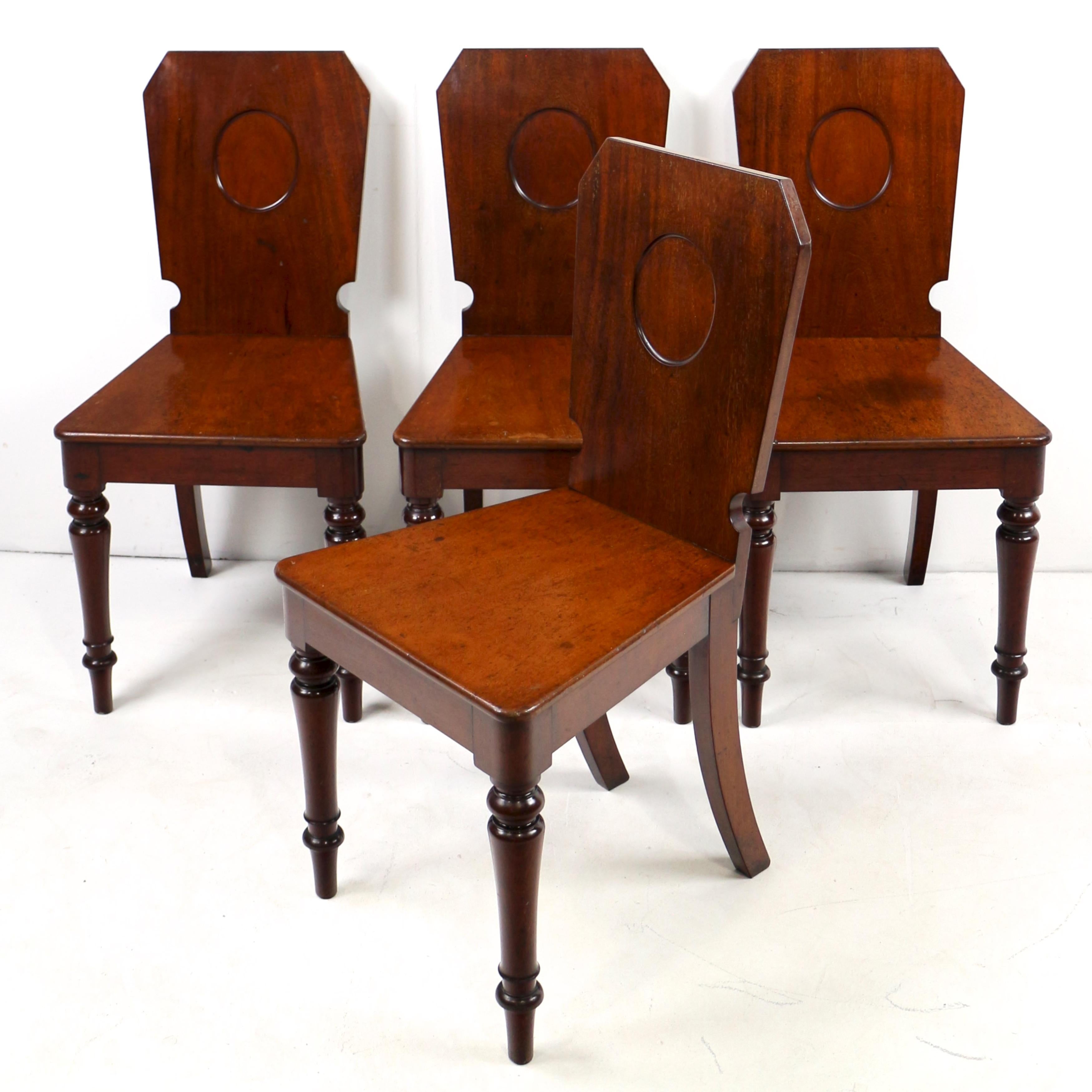 Un raro set di quattro sedie da sala in mogano del XIX secolo di Holland & Sons di Londra. Gli schienali squadrati a forma di scudo, ciascuno con un pannello ovale incassato libero sopra i sedili massicci, sono sollevati su gambe anteriori tornite e