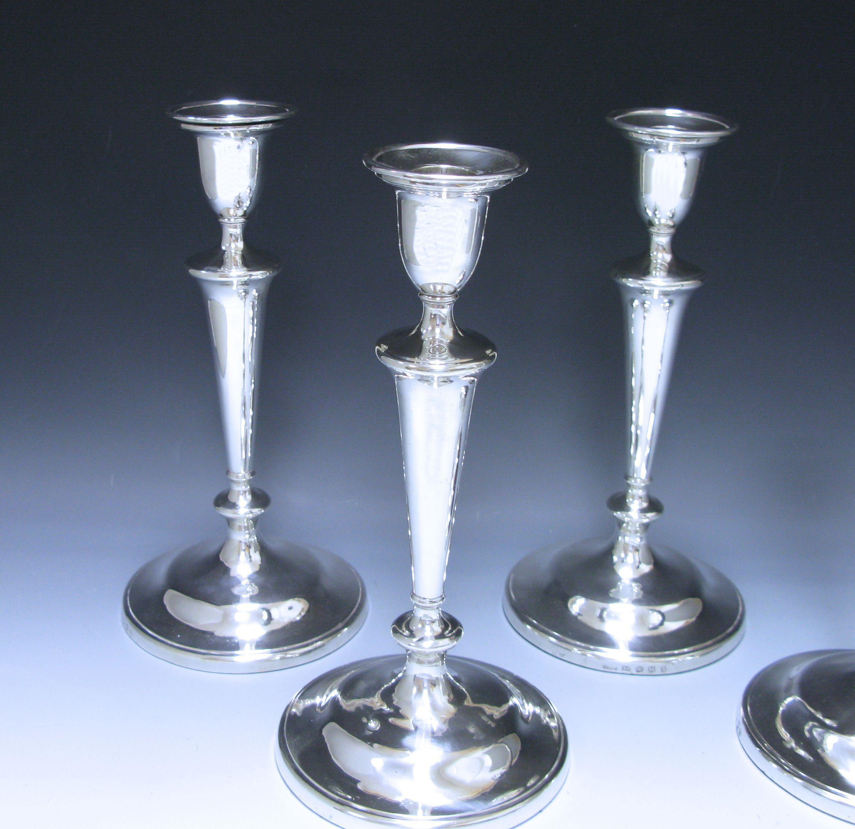 An impressive set of four antique George III sterling silver candlesticks which are plain and unembellished with bell shaped capitals. Each candlestick retains the original hallmarked push fit sconce, with a moulded rim. The columns are V-shaped and