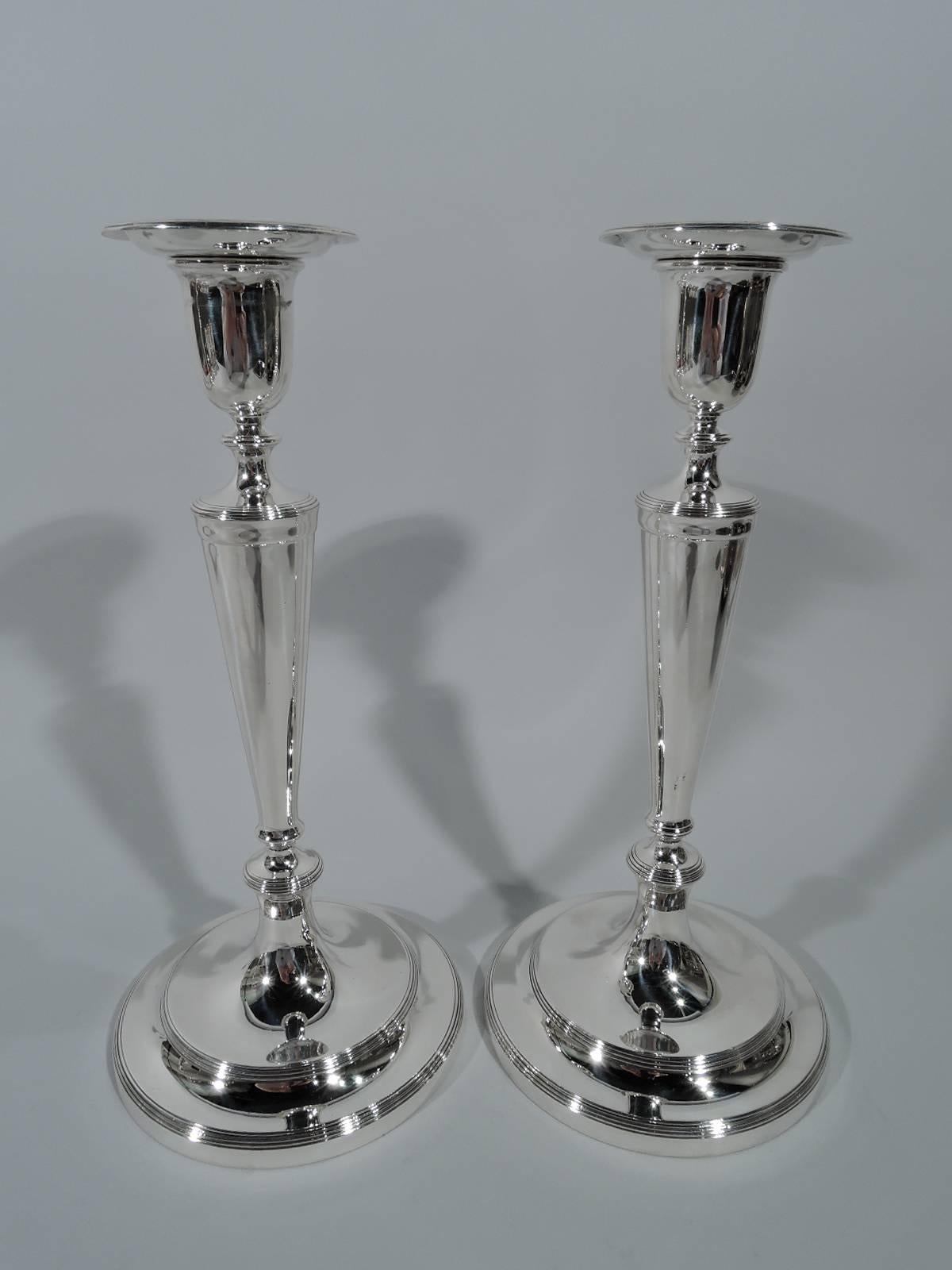 Four Edwardian Classical sterling silver candlesticks. Made by Tiffany & Co. in New York. Urn socket with detachable bobeche, tapering columnar shaft, knops, and stepped foot. Spare form embellished with reeding. An elegant set that works on both