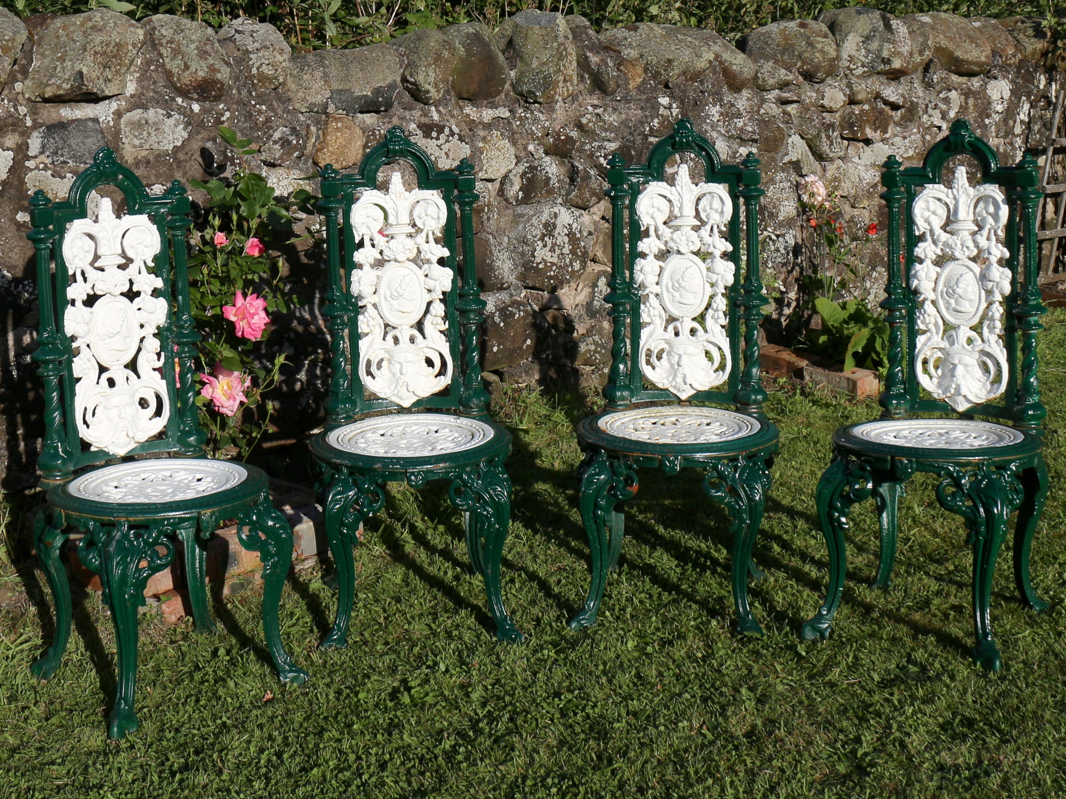 A set of four Victorian cast iron garden chairs dating to the late 19th century. The high backs an arched top and reeded and twisted uprights flanking a panel decorated with fruit and acanthus leaves surrounding a roundel with a classical profile