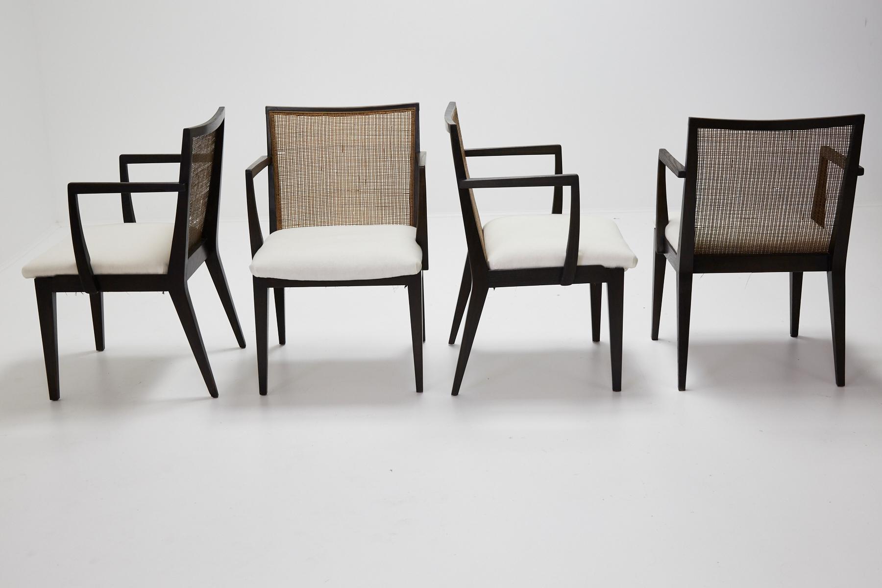 Set of four dining armchairs, model no. 5954 designed by Edward Wormley for Dunbar. Stained oak frames retain original caned backs. Seats have been reupholstered in muslin and ready for your specific fabric choice. Chairs retain brass Dunbar label