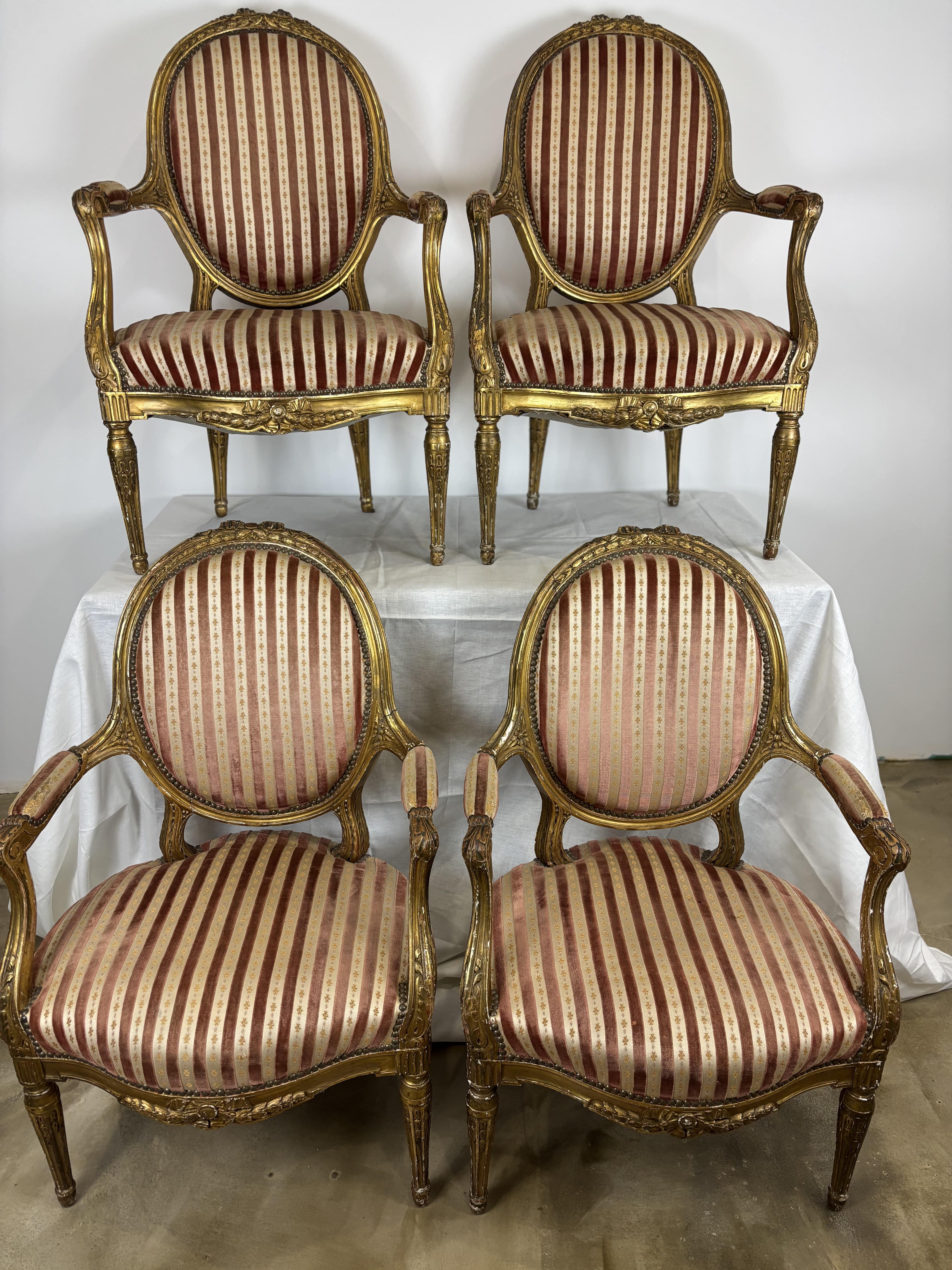 Set di quattro poltrone del XIX secolo in legno dorato e intagliato con motivi floreali e fogliati, schienale a medaglione, gambe scanalate e affusolate. Doratura patinata dal tempo. Struttura solida e stabile Doratura originale con segni di usura