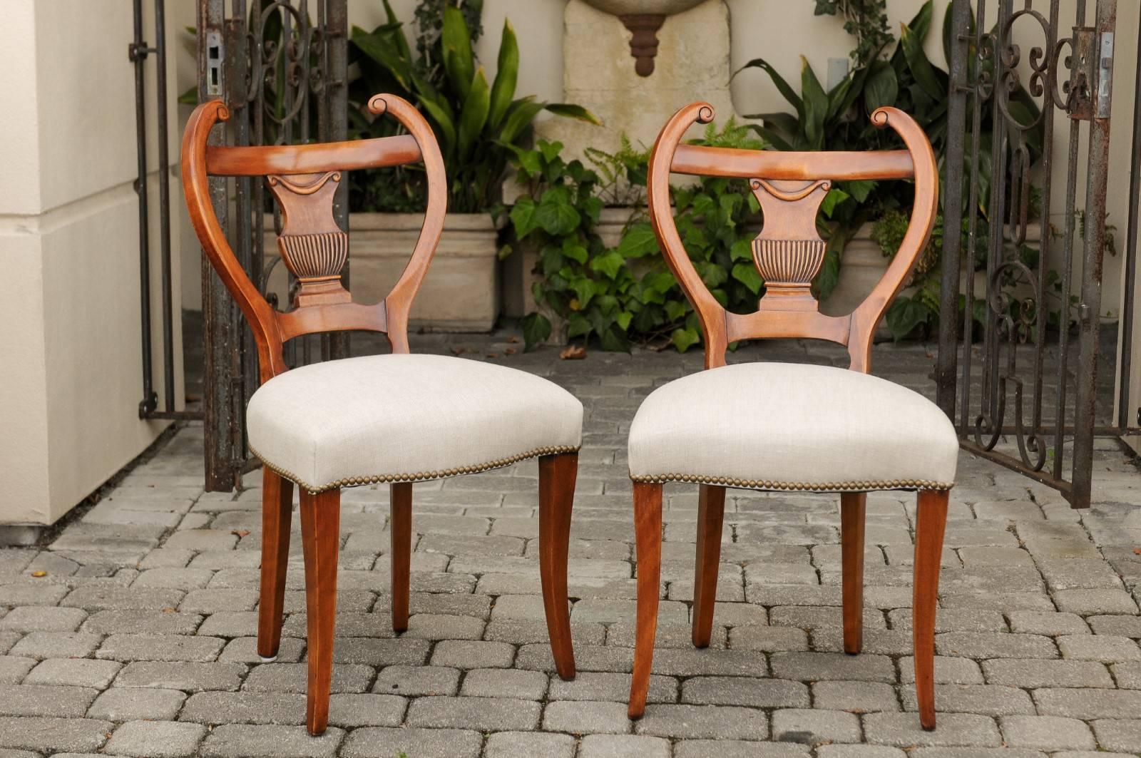A set of four Austrian Biedermeier dining chairs from the mid-19th century, with lyre-shaped backs, carved urns and new upholstery. Each of this set of Biedermeier side chairs features an exquisite lyre-shaped back, adorned with a carved splat