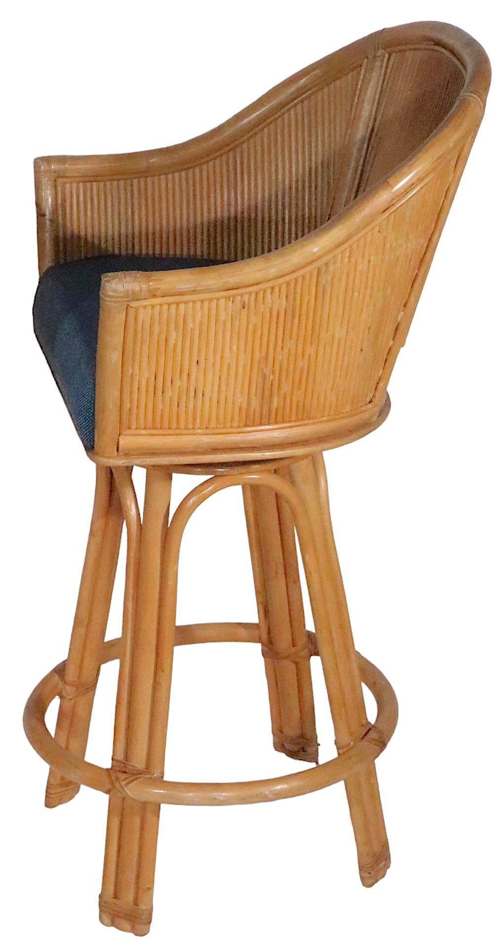 Casual, voguish and chic set of four counter height swivel bar stools, having a reeded scoop back rest, upholstered pad seat, and tall bamboo legs. The stools are in good, original, vintage, estate condition, showing only light cosmetic wear, normal