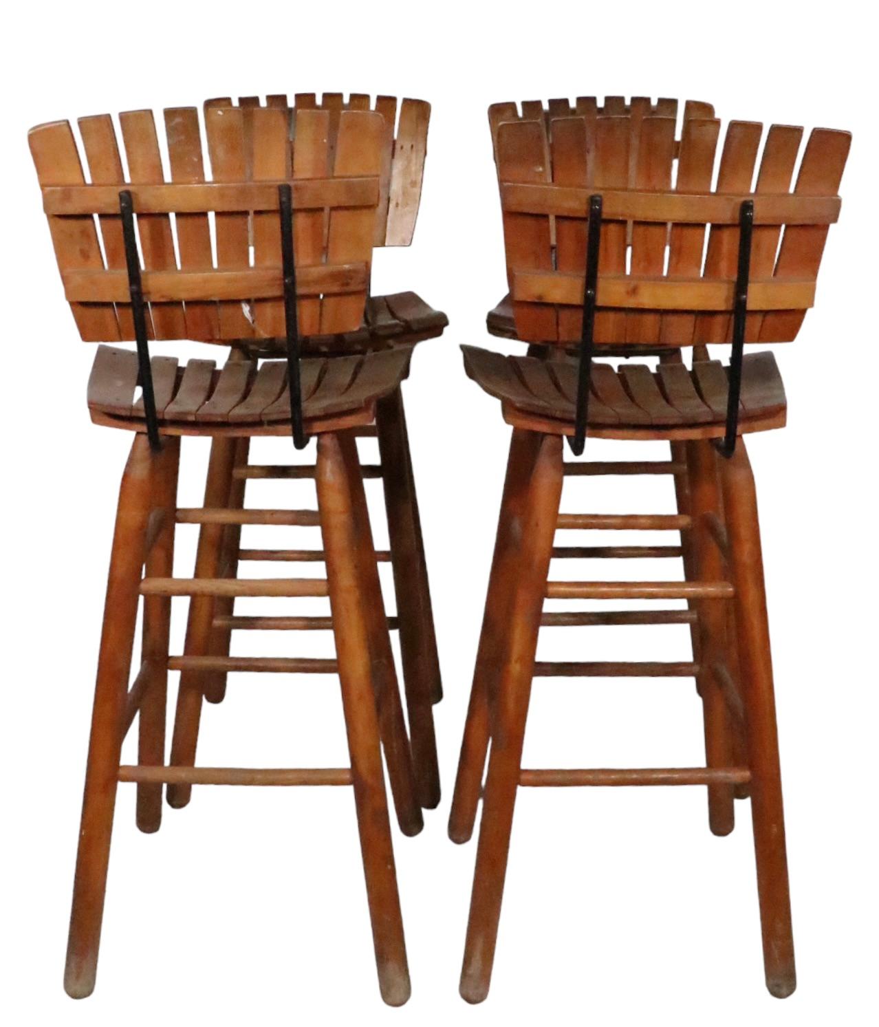 Unusual set off bar height stools designed by Arthur Umanoff, circa 1950's. The stools feature slatted backs and seats with solid wrought iron frames, on dowel form legs with exposed stretchers. All four are structurally sound and sturdy, all show