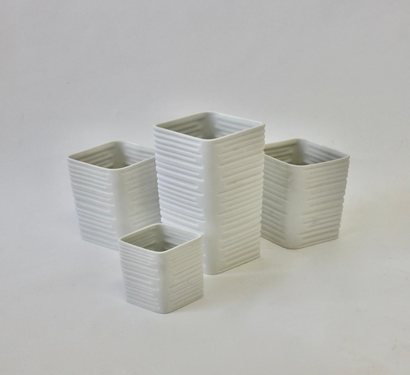 Ensemble de quatre vases en biscuit blanc. Deux sont assortis, l'un plus grand, l'autre plus petit. Ouverture en forme de diamant avec un motif de lignes incisées sur le corps, donnant à l'ensemble un aspect architectural.