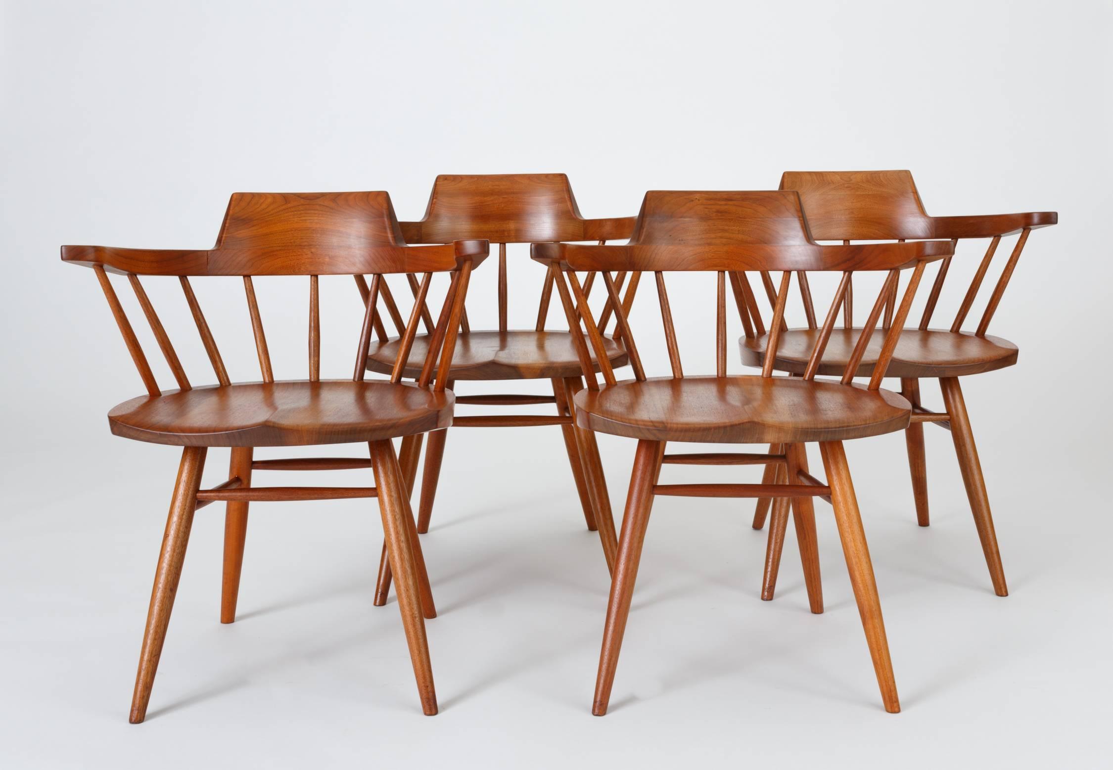 An accomplished set of four captain chairs from American midcentury craftsman George Nakashima. The black walnut chair has a curved, peaked backrest atop carved spindles, inspired by the Windsor chair and Shaker pieces. The seat is hand-sculpted for