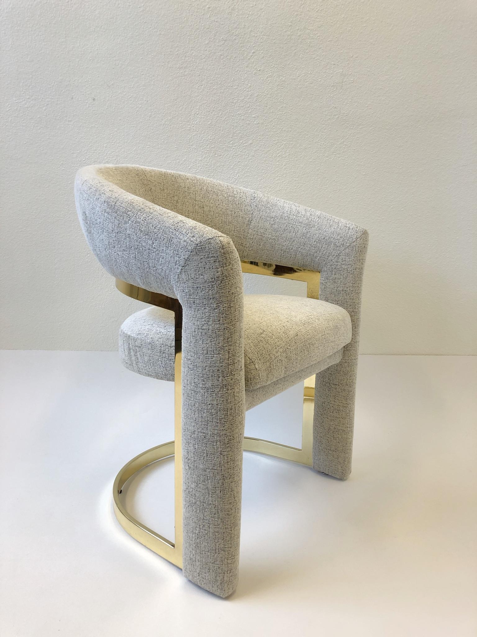 A set of four glamorous polish brass dining chairs designed in the 1980s by Design Institute of America. The chairs have been newly recovered in a soft off white with hints of light brown threads chenille tweed fabric. The brass is in original