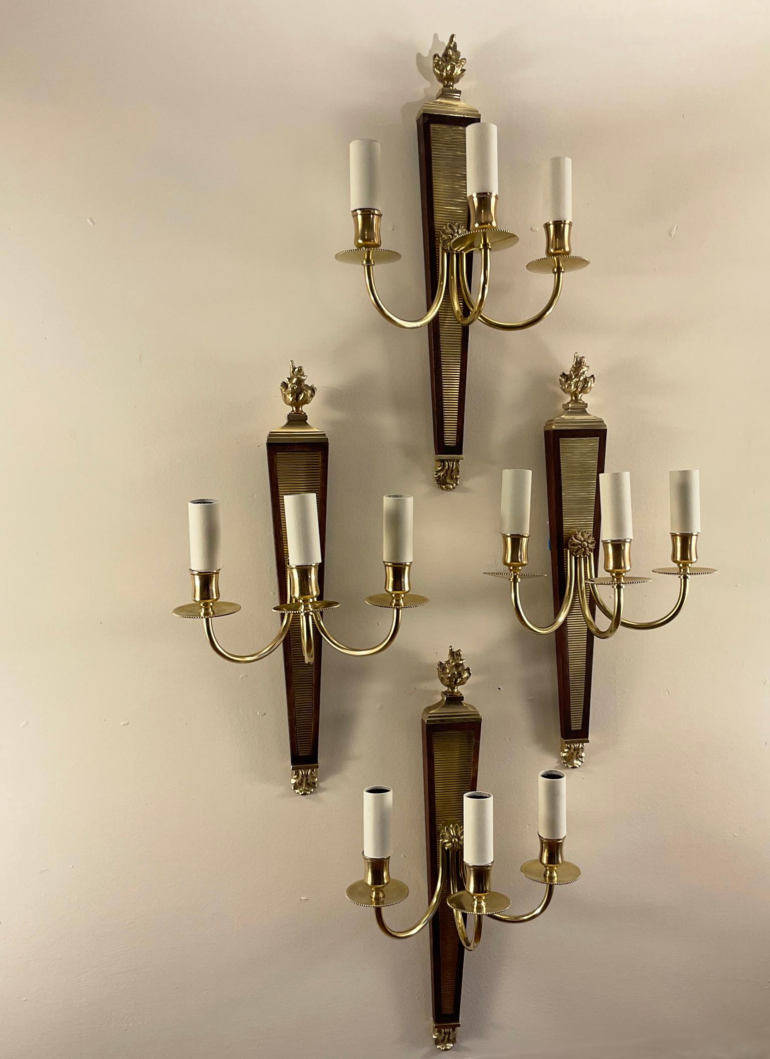 The 1940s set of four wall lights attributed to André Arbus (1903-1969) in gilded brass and mahogany.
Mahogany support with fluted brass base, from which three arms of light rise, ending in brass ornamental torches.