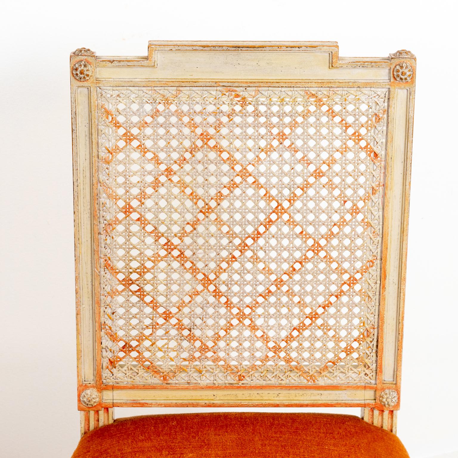 Set of four caned and painted side chairs with latticework on the rectangular seat back and metal nail head trim. The piece also features upholstered seats and fluted, turned legs. Please note of wear consistent with age including minor paint loss
