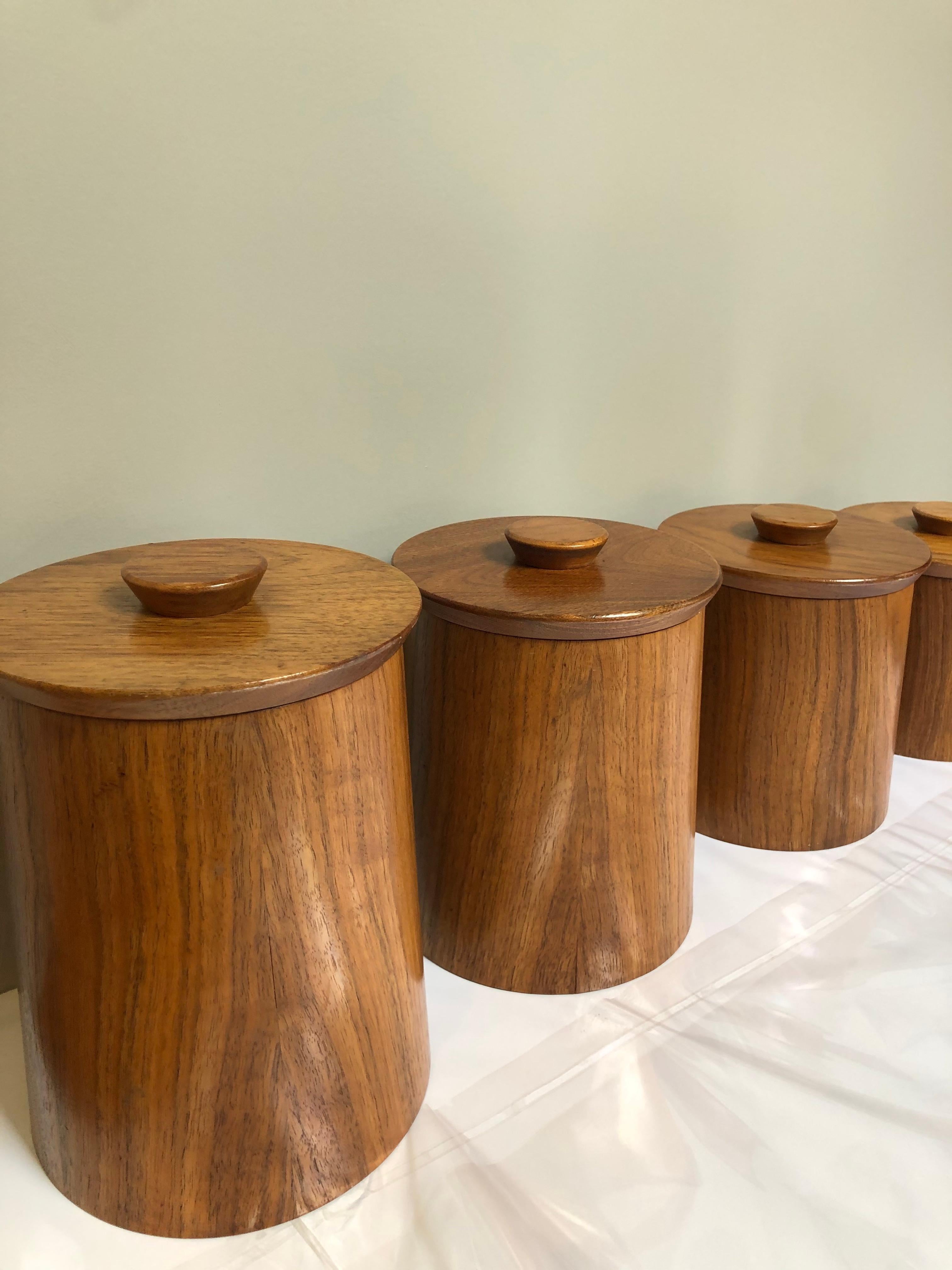 This set of 4 canisters merge functionality with modern aesthetics. These canisters would serve as well on a desk as on shelves in a library. They have lids of graduating sizes in teak. (Size noted is that of largest canister).