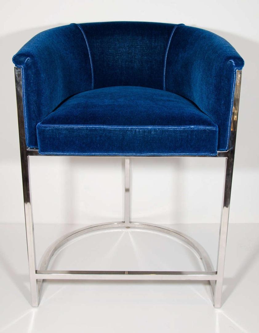 These classic barrel back design bar stools were designed in the 1970s in the style of Milo Baughman. Re-upholstered in blue velvet on chrome frames with connecting footrest for maximum comfort. They are a versatile size and can be used as bar