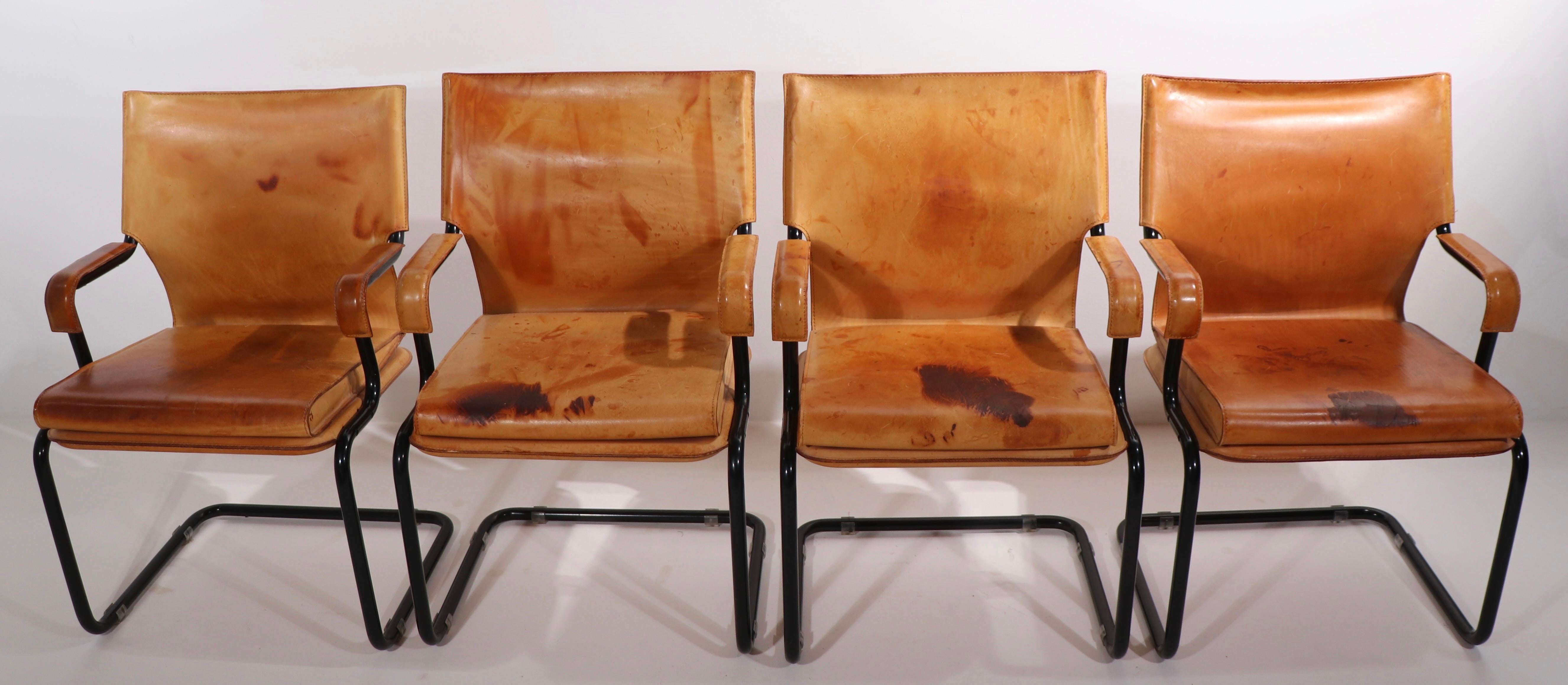 Iconic Uno chairs designed by Paolo Deganello and Gilberto Coretti of Archizoom. Set of four, in brown saddle leather on tubular black metal cantilevered frames. Three of the four have significant stains, my guess is a red wine spill. All are