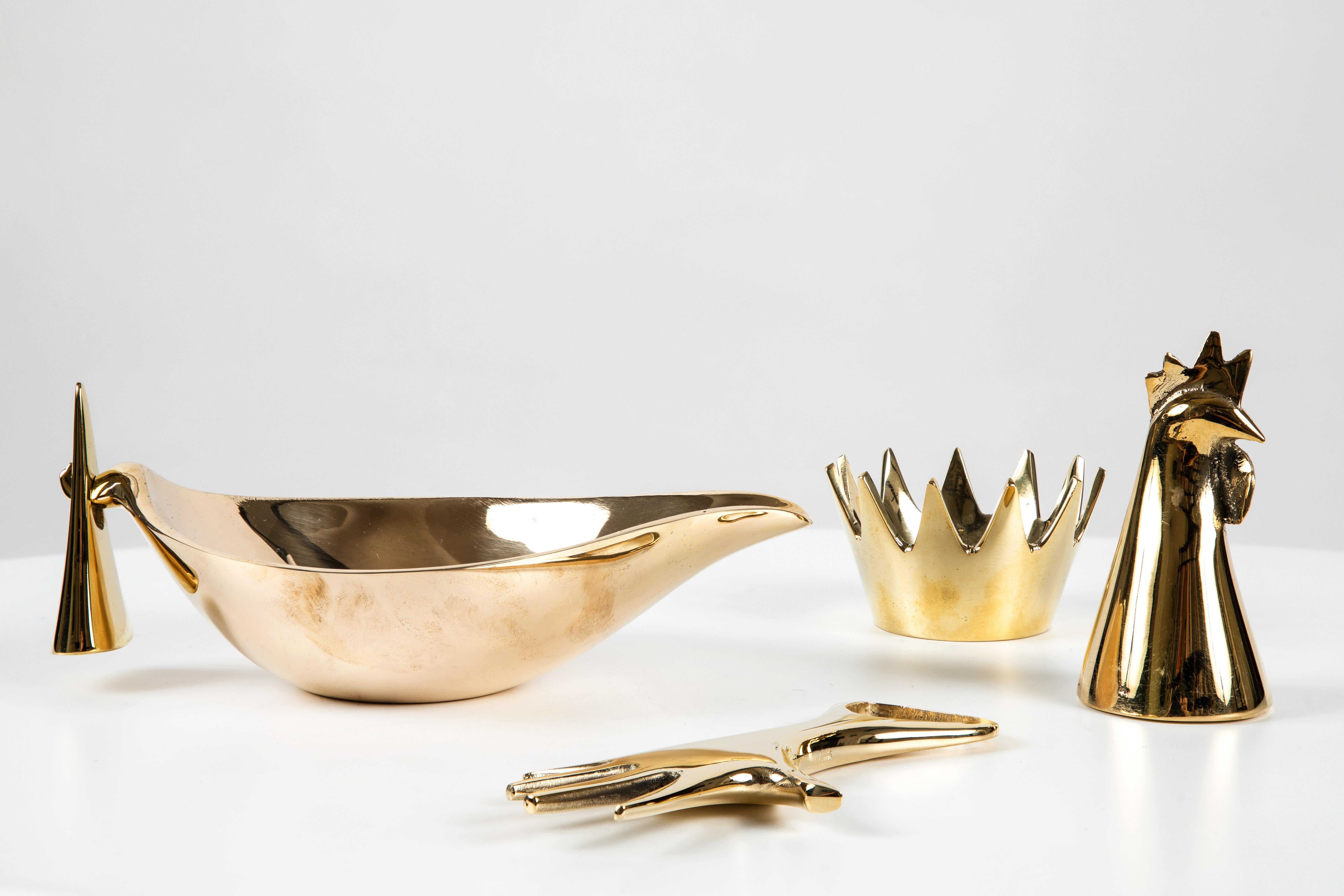 Set of four Carl Auböck brass objects. Includes Carl Auböck model #4072/G 'Rooster' brass bell, model #3600 'Crown' brass bowl, model #3514 brass bowl and model #4224 'Hand' brass bottle opener. Designed in the 1950s, these incredibly refined and
