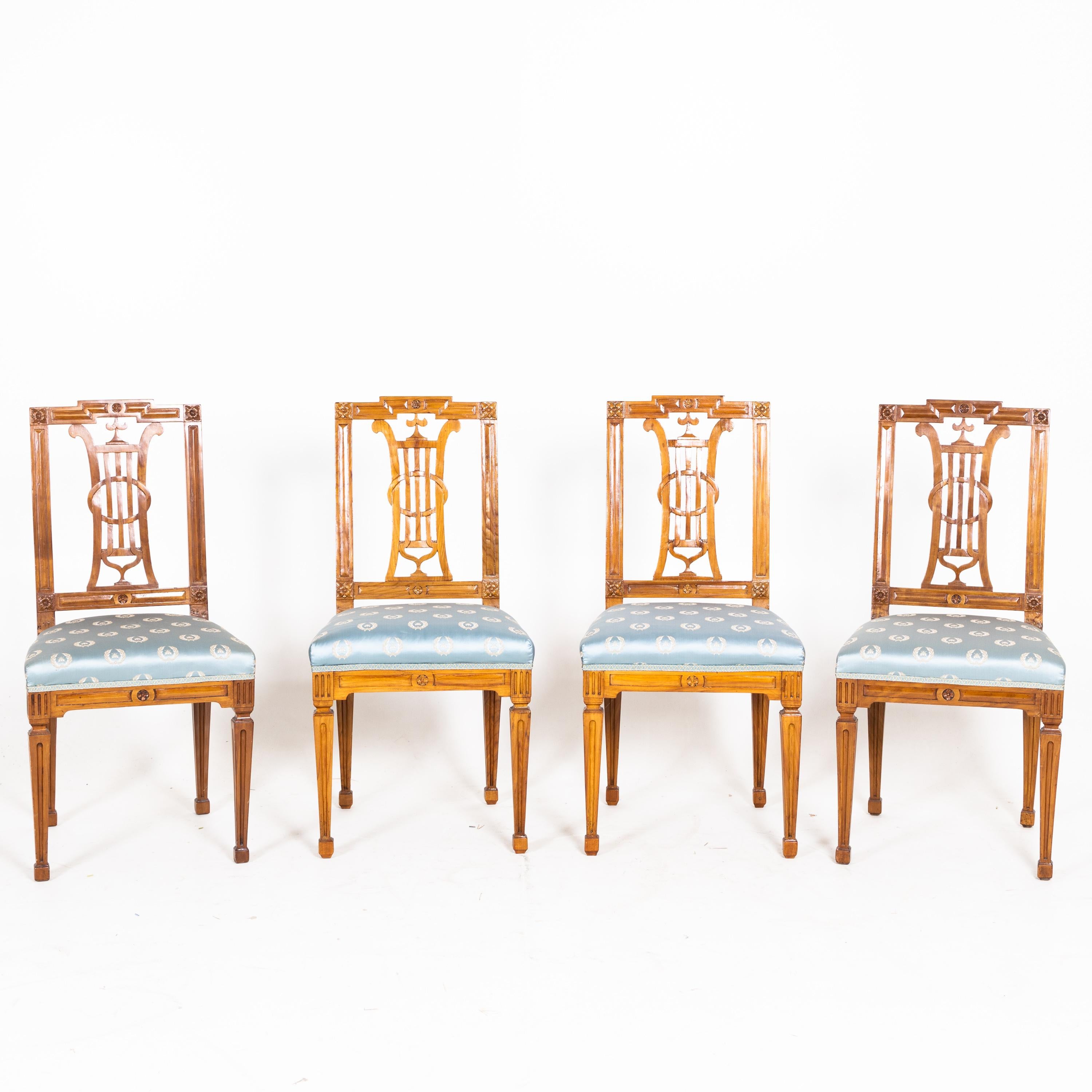 Set of four chairs on fluted tapered legs with carved frames and openwork backrests with harp ornaments. The seats are covered with light blue satin fabric with embroidered bee and laurel wreath decoration in gold. Carved solid cherry. Shown in: