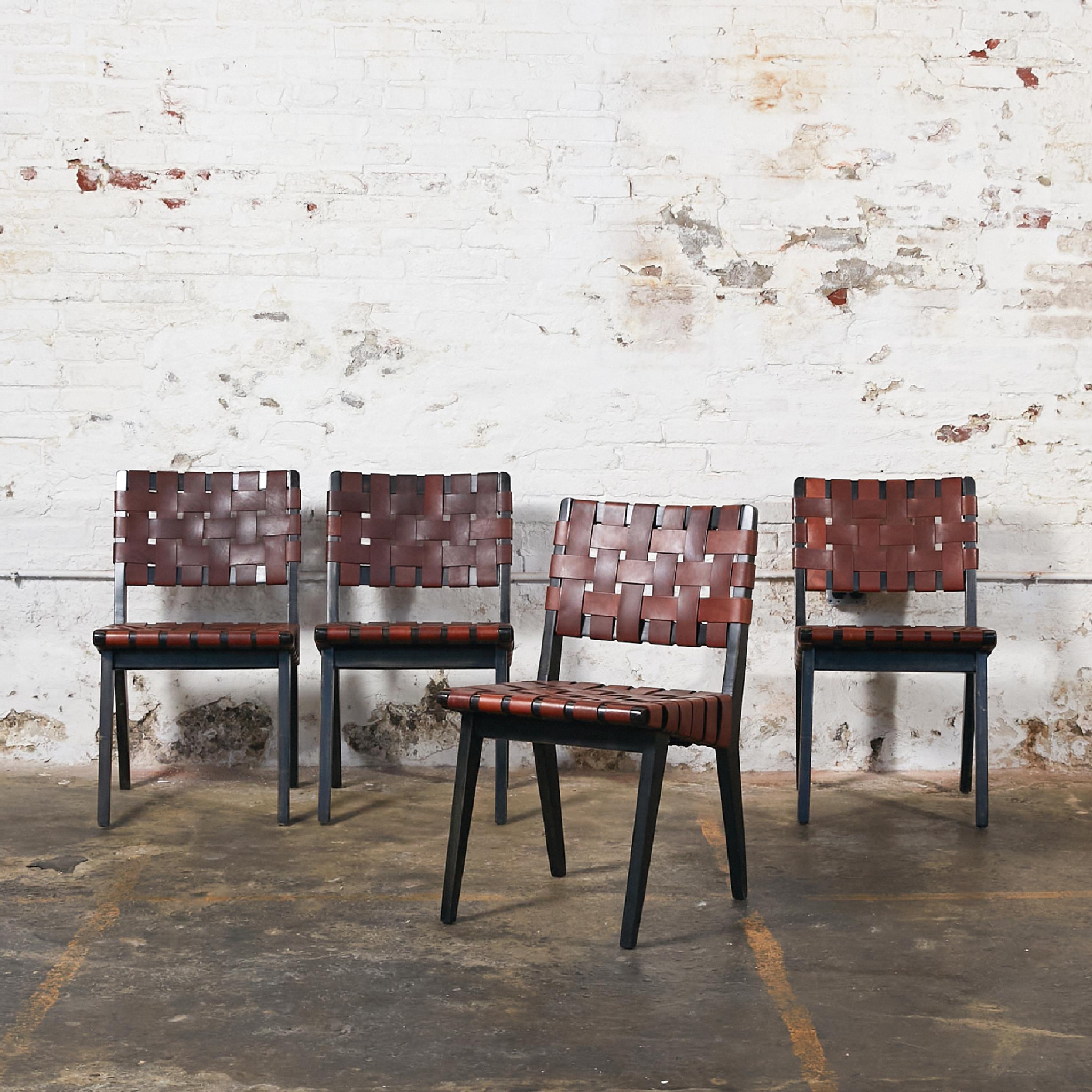 Set of four chairs in the style of Jens Risom.
Frame in wood stained in black. Seat and back in woven saddle brown leather straps, with studs in antique bronze finish.