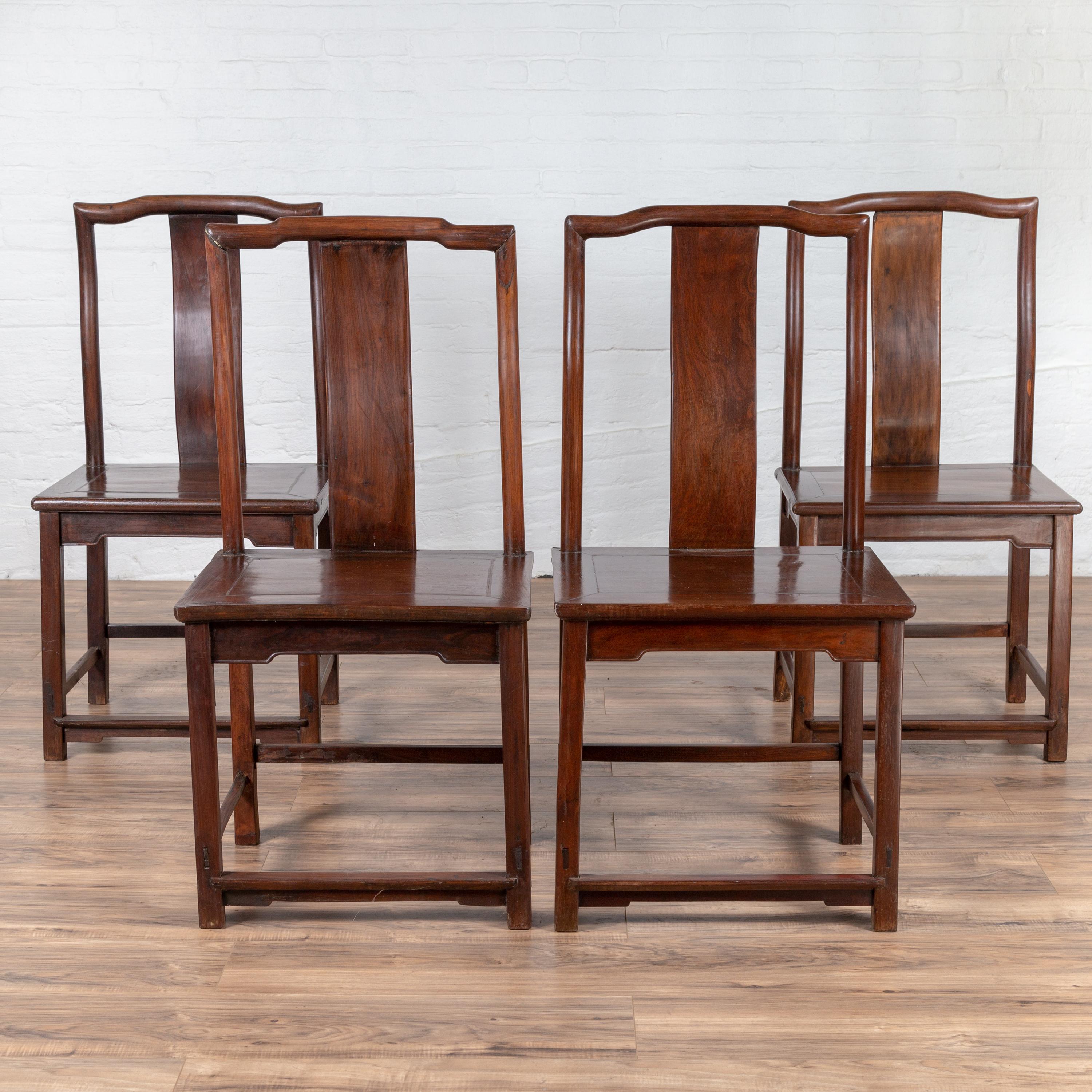 A set of four antique Chinese elmwood scholar's ceremonial side chairs from the early 20th century, with dark patina and sinuous back splats, all with slight variations. Born in China during the early years of the 20th century, each of this set of