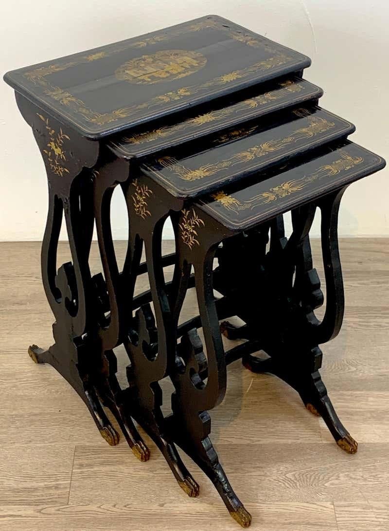 A fine set of four antique, ebonized Chinese export nesting tables produced in the mid-19th century. Graduated in size, each lacquered wood table is masterfully gilt-painted in traditional Chinoiserie scenes and motifs, and the lyre supports and paw