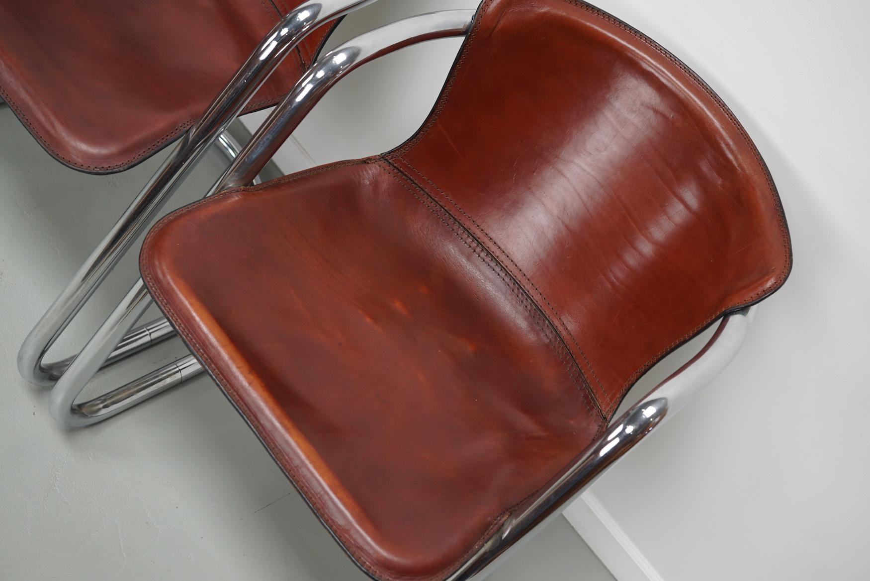 This set of four dining chairs were designed by Willy Rizzo in the 1970s. They feature a chrome tubular frame with thick cognac leather seats. They are in a good vintage condition with signs of use.