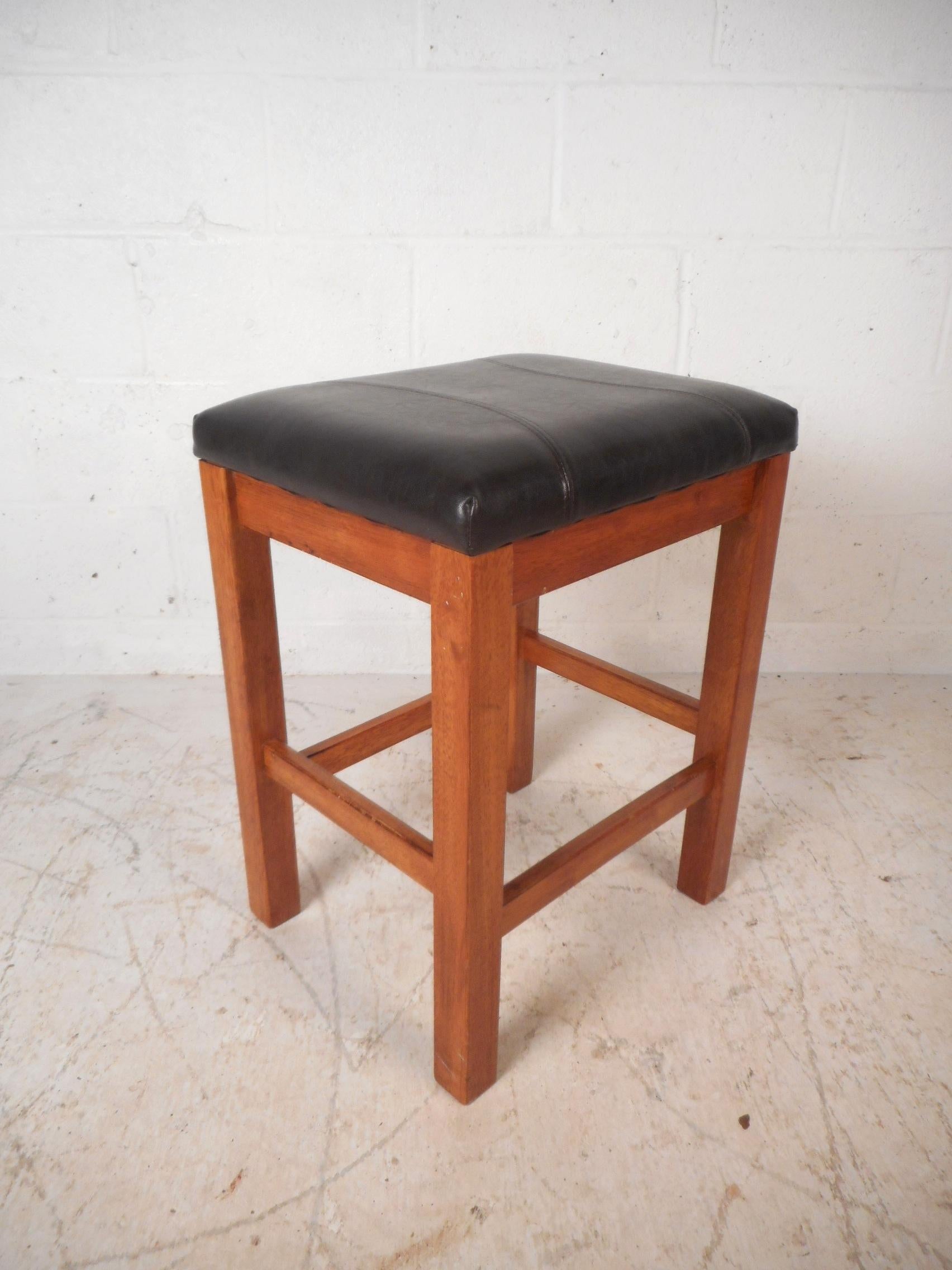 This beautiful set of four midcentury style bar stools feature a thick padded seat covered in stitched black vinyl. A straight line design with a sturdy walnut frame and a conveniently placed kick rest for maximum comfort. This stunning set makes