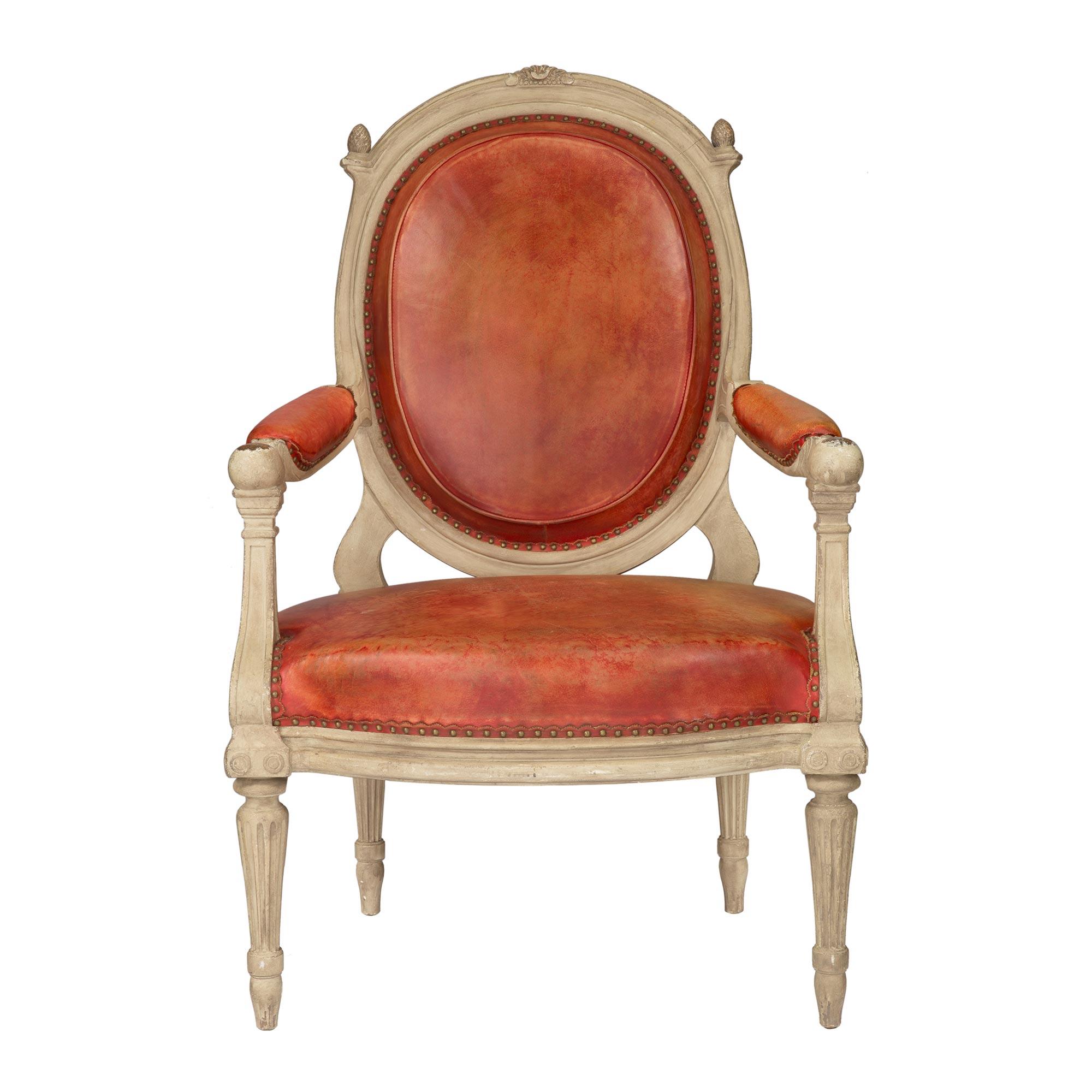 A striking and complete set of four Continental 19th century Louis XVI style patinated wood and red leather armchairs. Each beautiful chair is raised by elegant circular tapered fluted legs with finely carved topie shaped feet. Above each leg are