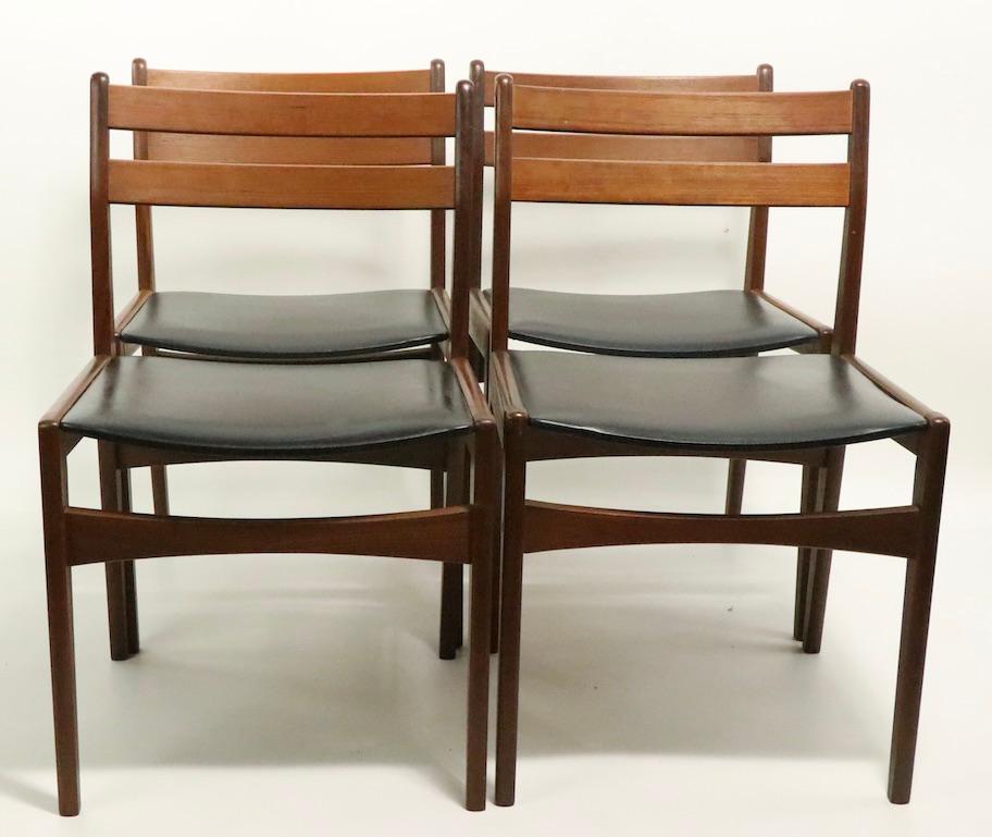 Set of four midcentury Danish modern dining chairs, made by Frem Rojle and retailed by Bon Marche NYC. Dark teak frames with black vinyl scoop form seats. All four are in very Fine, original condition, clean, solid, sturdy and ready to use