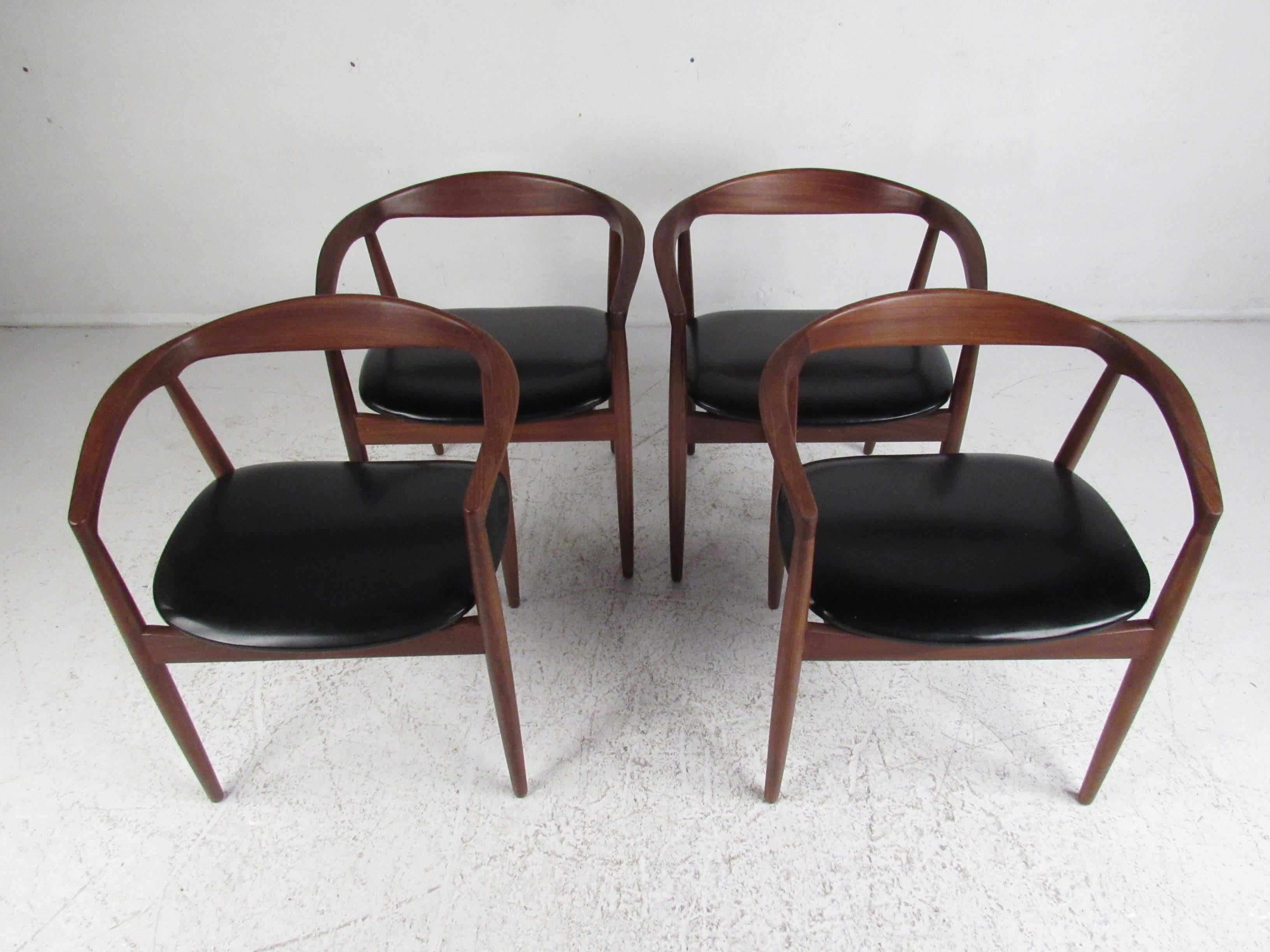 This stunning set of four Mid-Century Modern armchairs boast sculpted teak frames and black vinyl covered seats. A sleek design with a barrel backrest, sloped arm rests, and tapered legs. This gently used set of dining chairs make the perfect