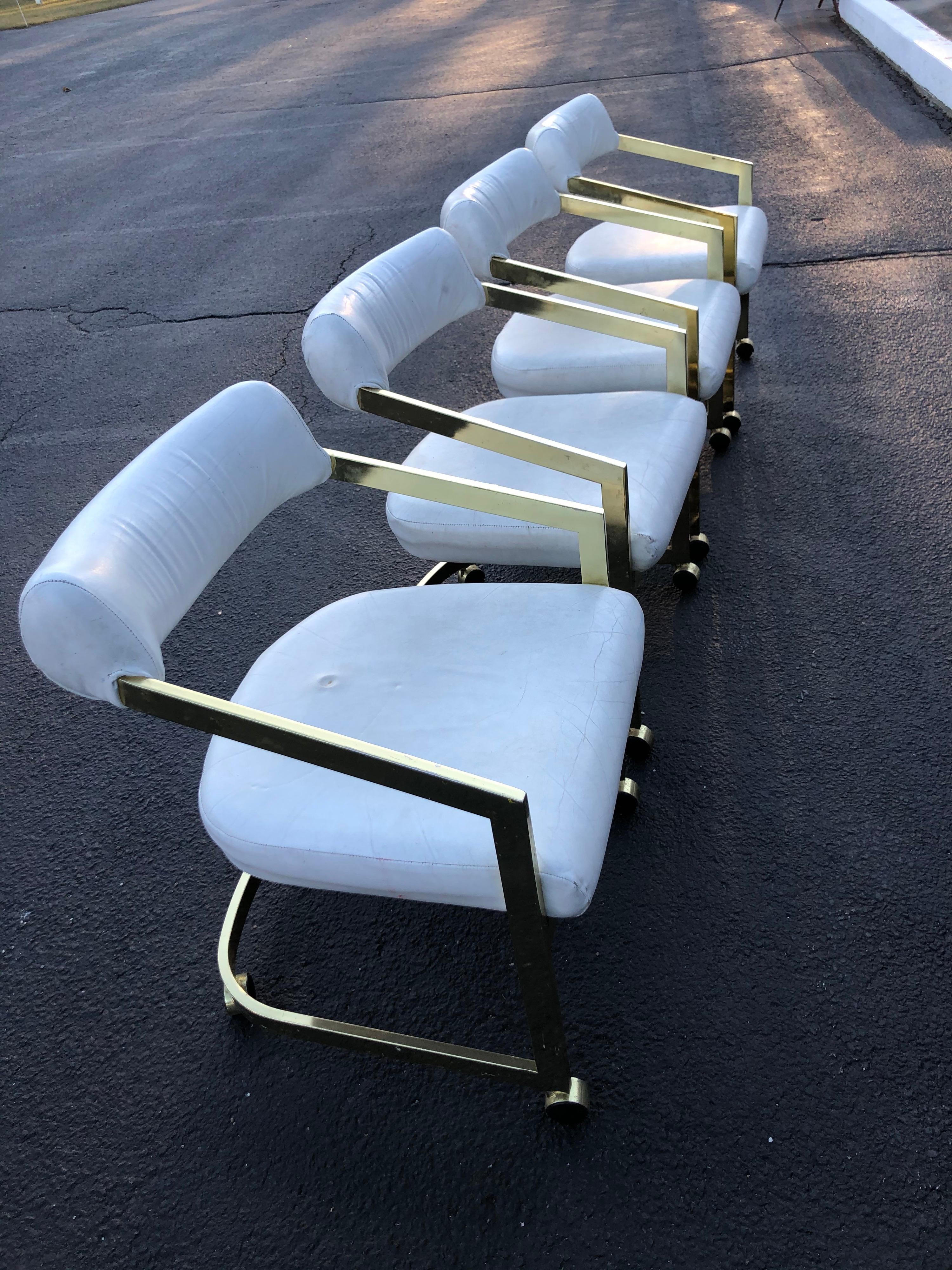 Set of four design institute of America chairs. White leather and plated brass. On castors. Use in an office or for dining. Sleek, sexy design. Super comfortable. Seat depth is 20 and seat height is 19