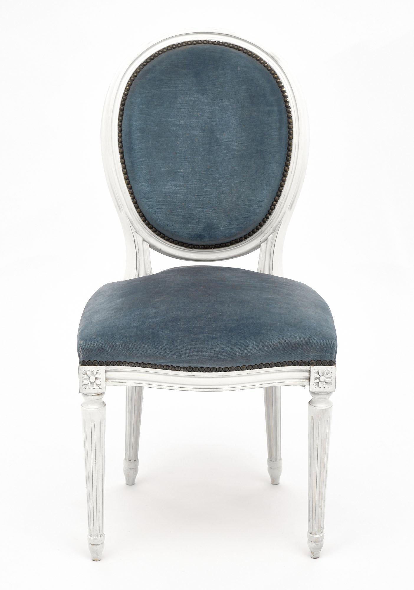 Set of four chairs from France in the Louis XVI style made with hand-carved and painted beech wood frames. The original upholstery is blue velvet and in good condition with only minor wear consistent with age. We love the hand-carved details and