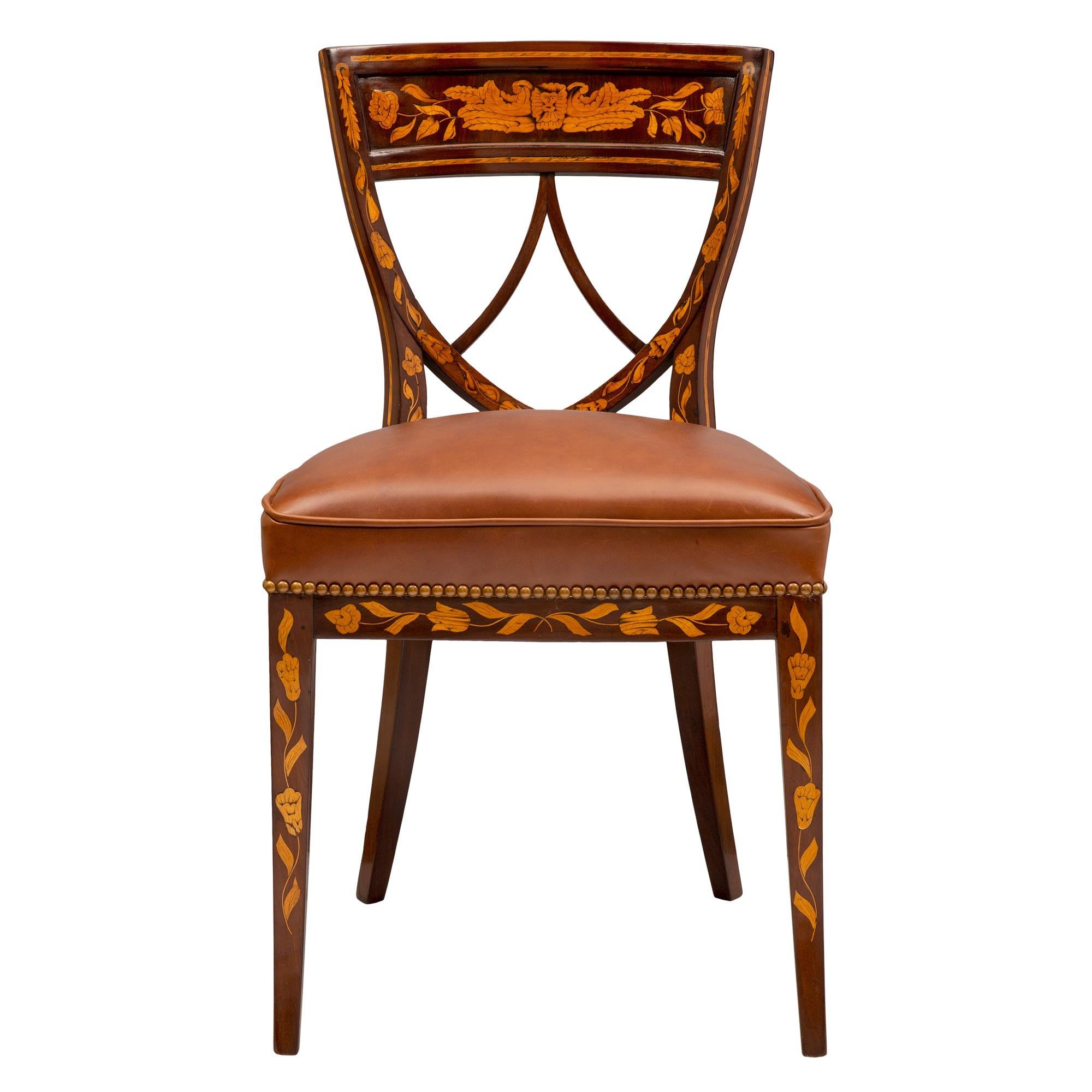 An exceptional and complete set of four Dutch 19th century Louis XVI style mahogany, walnut, and maple wood side chairs. Each beautiful chair is raised by elegant lightly curved mahogany legs with finely inlaid maple foliate designs. The superb