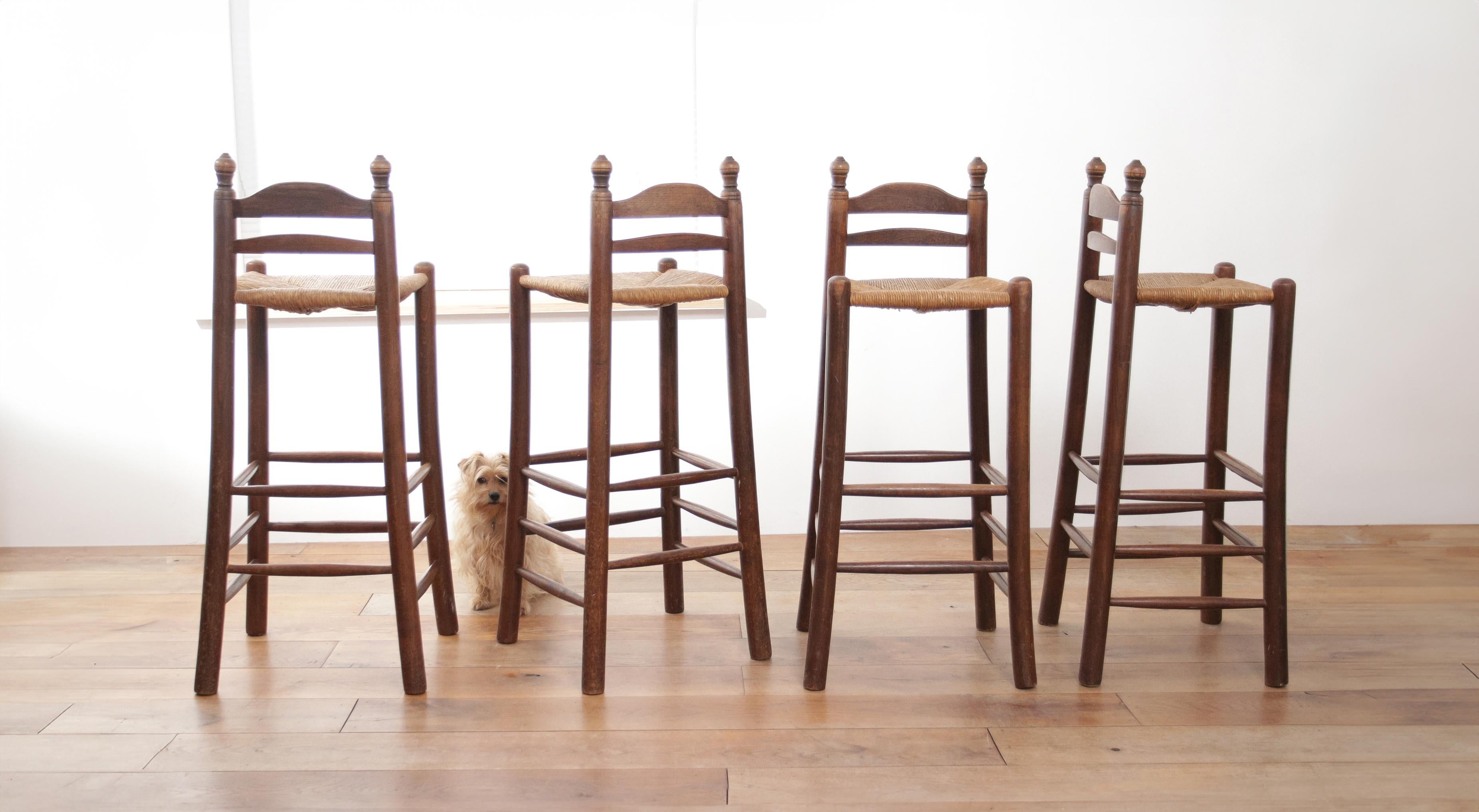 These solid oak barstools have a traditional Dutch design, and are made around 1960. They have a classic silhouette with vertical slats on the backrest, turned legs, and crossbars that also serve as footrests. The seats are woven with rush, which